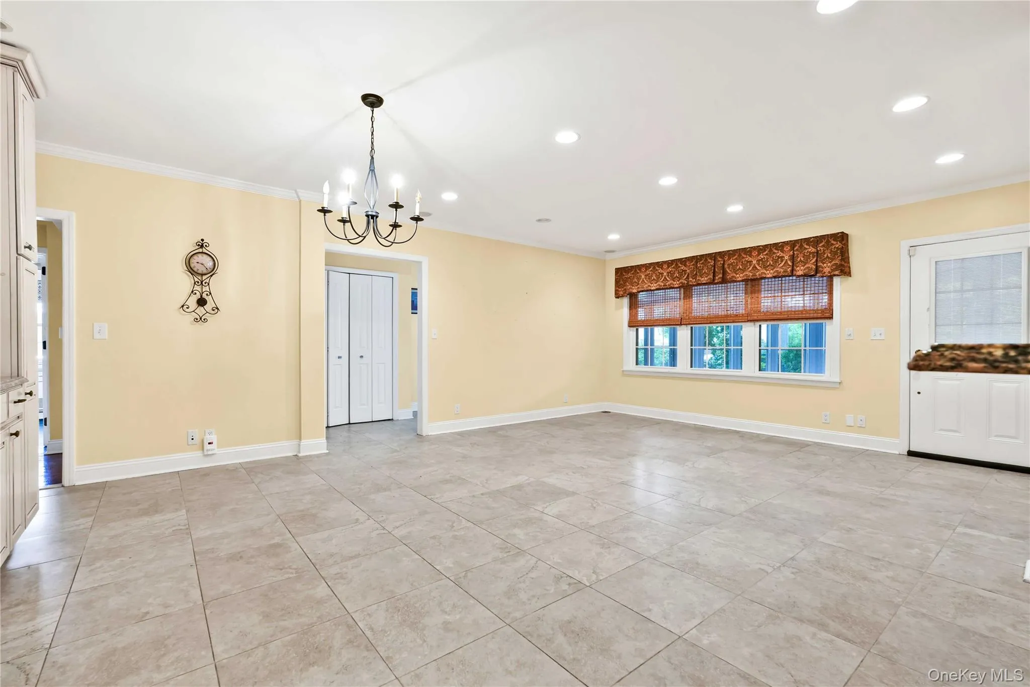 Spacious room featuring neutral-toned tile flooring, recessed lighting, and a prominent chandelier Spacious room featuring neutral-toned tile flooring, recessed lighting, and a prominent chandelier