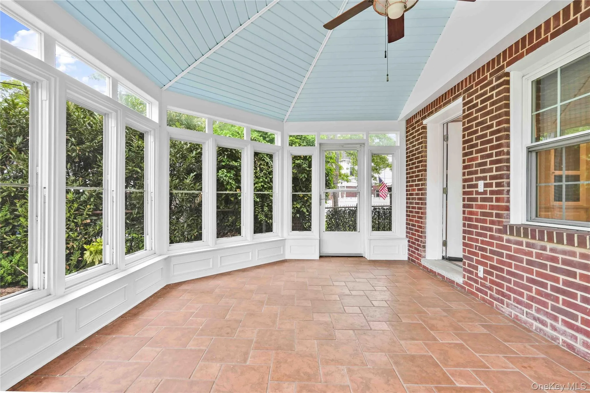 Sunroom featuring extensive window arrays, vaulted beadboard ceiling, terracotta-hued tile flooring, and direct access to the brick exterior Sunroom featuring extensive window arrays, vaulted beadboard ceiling, terracotta-hued tile flooring, and direct access to the brick exterior