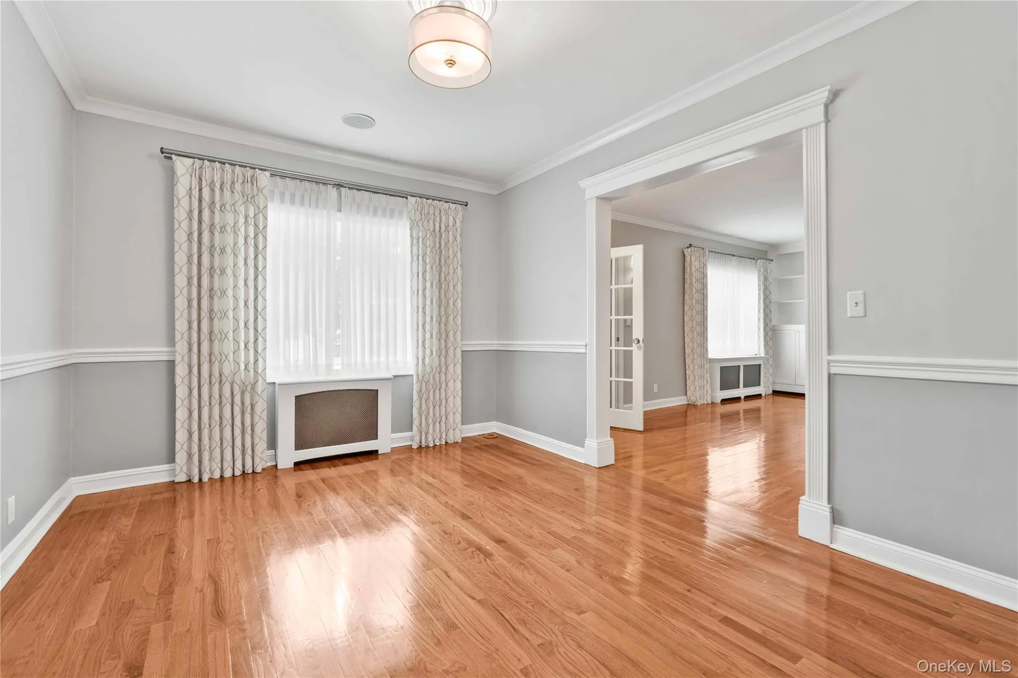 Spacious interior featuring wood-finish flooring, two-tone wall paint with wainscoting, crown molding, and an arched doorway Spacious interior featuring wood-finish flooring, two-tone wall paint with wainscoting, crown molding, and an arched doorway