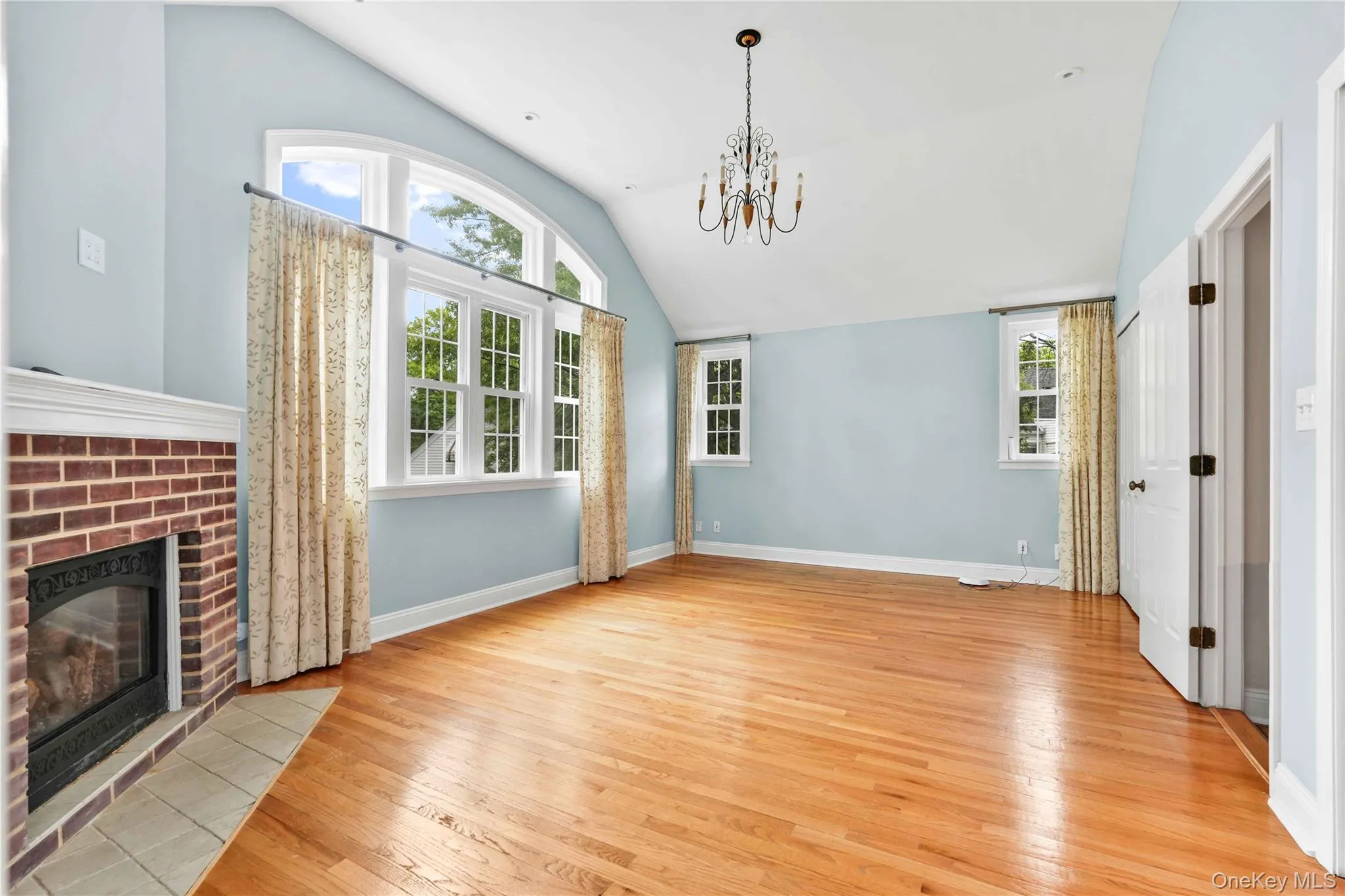 Main BedroomRoom featuring wood-finish flooring, a brick gas fireplace with a tile hearth, and vaulted ceilings. Tree views Main BedroomRoom featuring wood-finish flooring, a brick gas fireplace with a tile hearth, and vaulted ceilings. Tree views