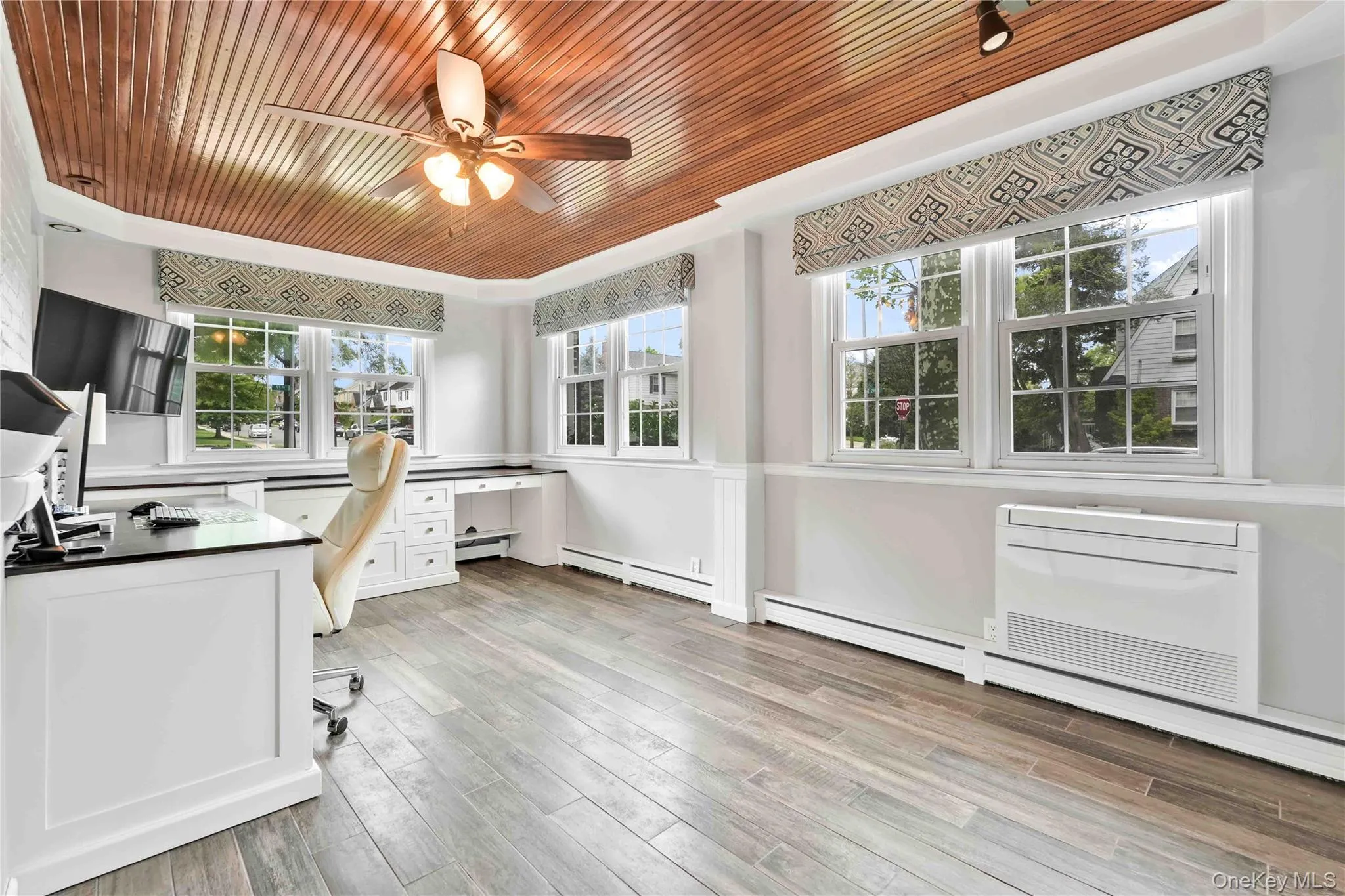 Room featuring a wood-panel ceiling with a ceiling fan, white paneled wainscoting, and porcelain wood look-finish flooring Room featuring a wood-panel ceiling with a ceiling fan, white paneled wainscoting, and porcelain wood look-finish flooring