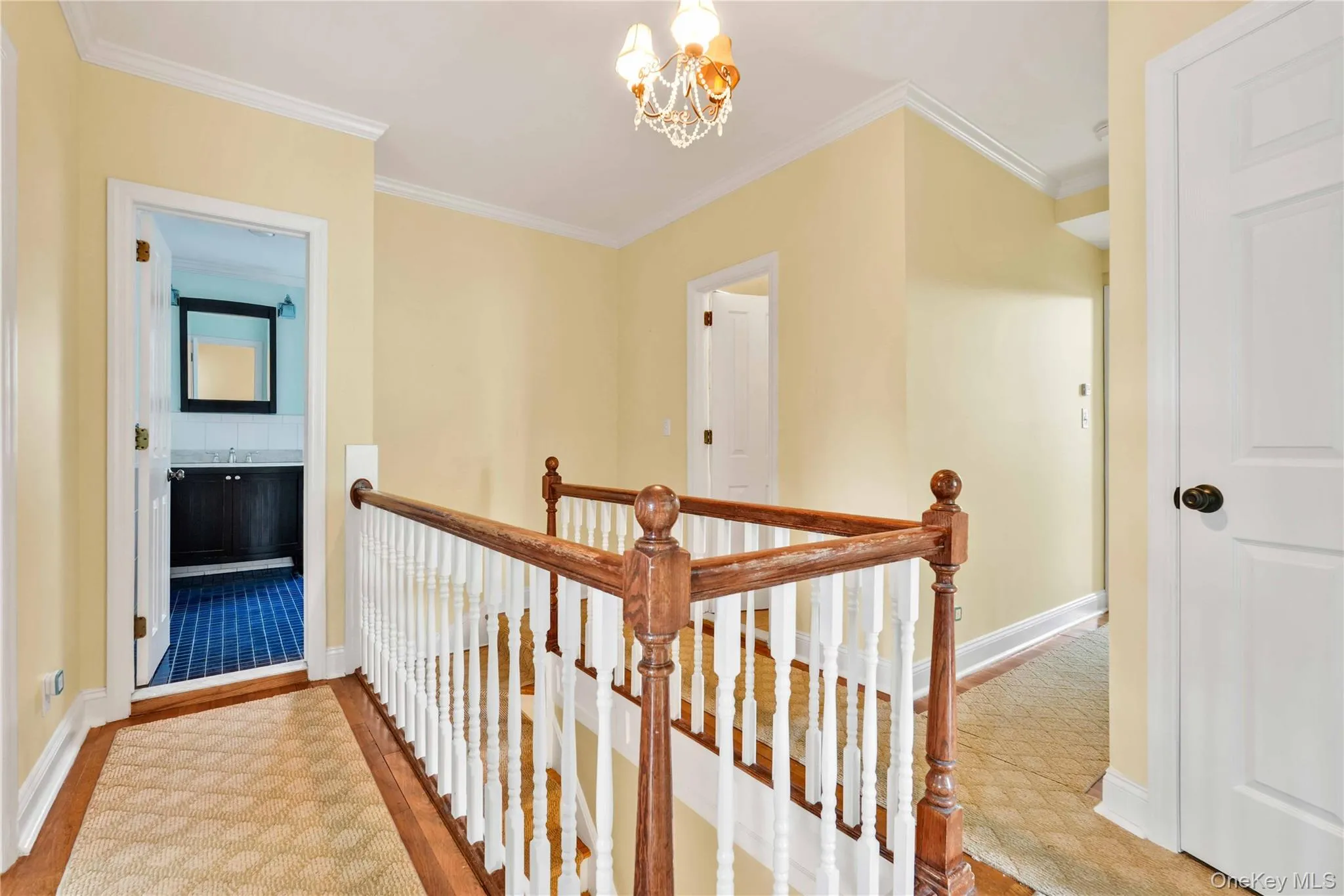 Upper landing with hardwood flooring, a detailed wood and white spindle staircase, crown molding, and a chandelier light fixture Upper landing with hardwood flooring, a detailed wood and white spindle staircase, crown molding, and a chandelier light fixture