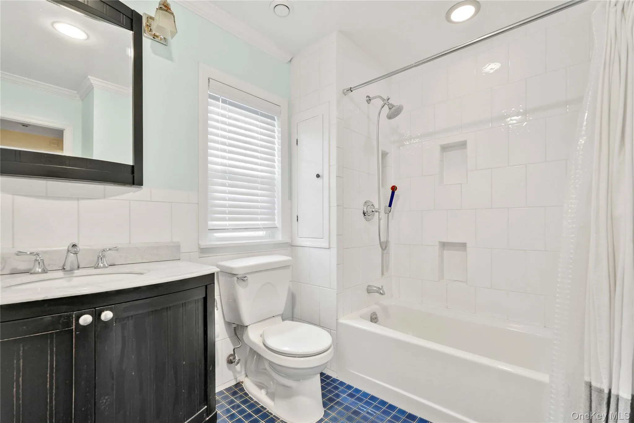 Bathroom featuring a dark wood-finish vanity with a light countertop, white subway tile wainscoting, and a window with blinds Bathroom featuring a dark wood-finish vanity with a light countertop, white subway tile wainscoting, and a window with blinds
