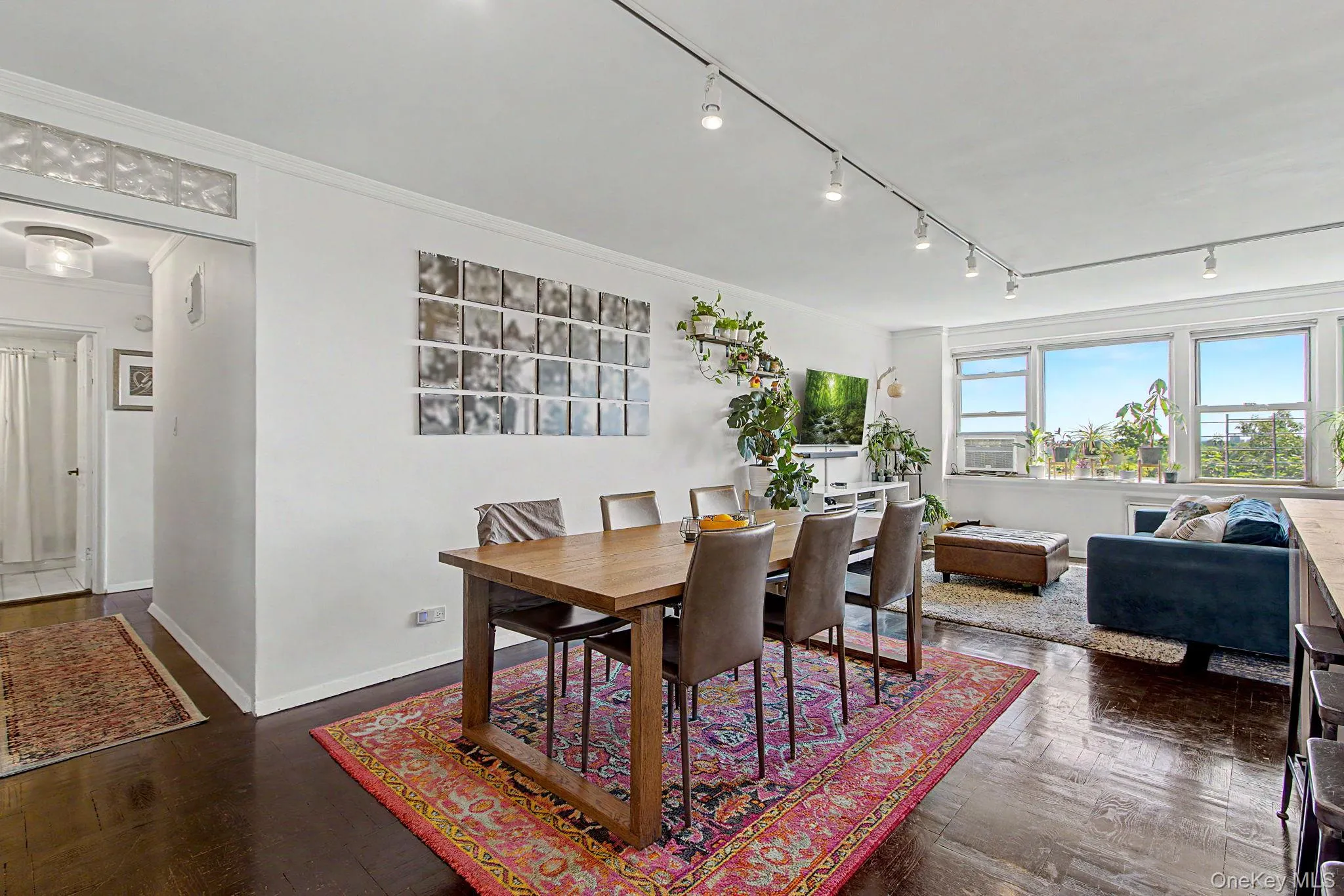 Spacious living and dining areas featuring dark wood-finish flooring, track lighting, crown molding, and large windows Spacious living and dining areas featuring dark wood-finish flooring, track lighting, crown molding, and large windows