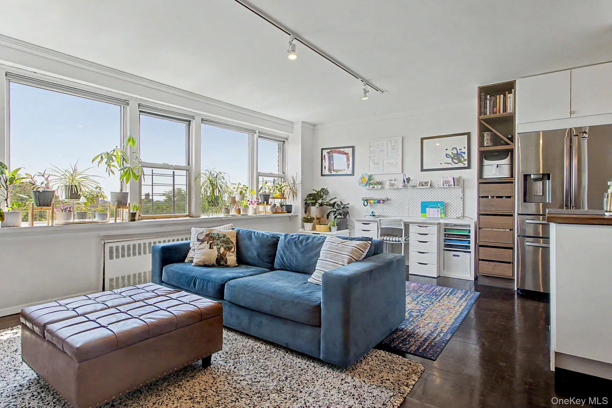 Living area featuring a wall of multiple windows, dark wood-finish flooring, and a built-in stainless steel refrigerator Living area featuring a wall of multiple windows, dark wood-finish flooring, and a built-in stainless steel refrigerator