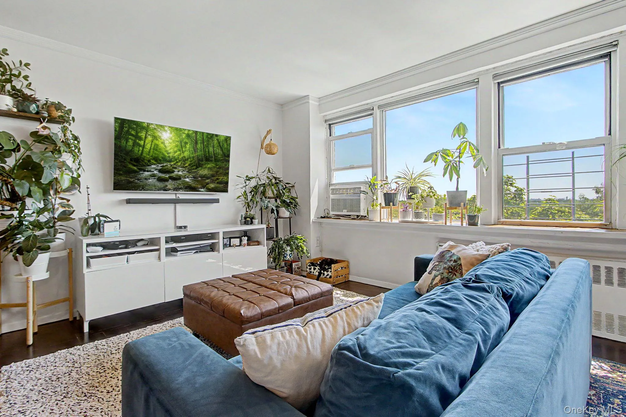 Bright living space featuring expansive windows, dark wood-finish flooring, white walls, and a built-in media console Bright living space featuring expansive windows, dark wood-finish flooring, white walls, and a built-in media console