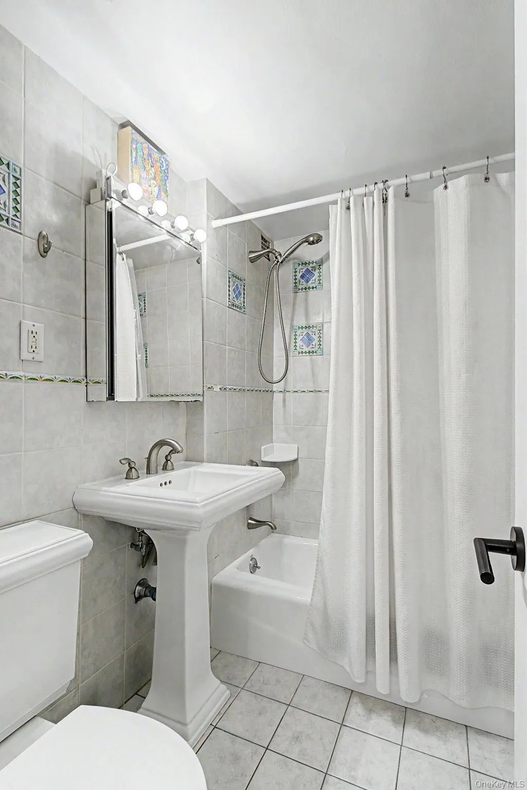 Bathroom featuring tiled walls, pedestal sink, chrome faucet, medicine cabinet, and a tiled shower/tub combination with a shower head Bathroom featuring tiled walls, pedestal sink, chrome faucet, medicine cabinet, and a tiled shower/tub combination with a shower head
