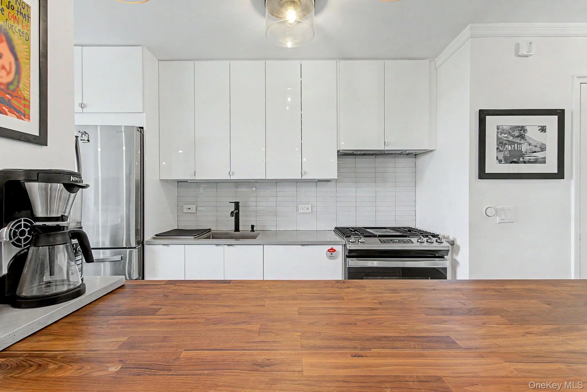 Kitchen featuring a wood-finish countertop, white cabinetry with polished hardware, stainless steel appliances, a gray countertop, and a white subway tile backsplash Kitchen featuring a wood-finish countertop, white cabinetry with polished hardware, stainless steel appliances, a gray countertop, and a white subway tile backsplash