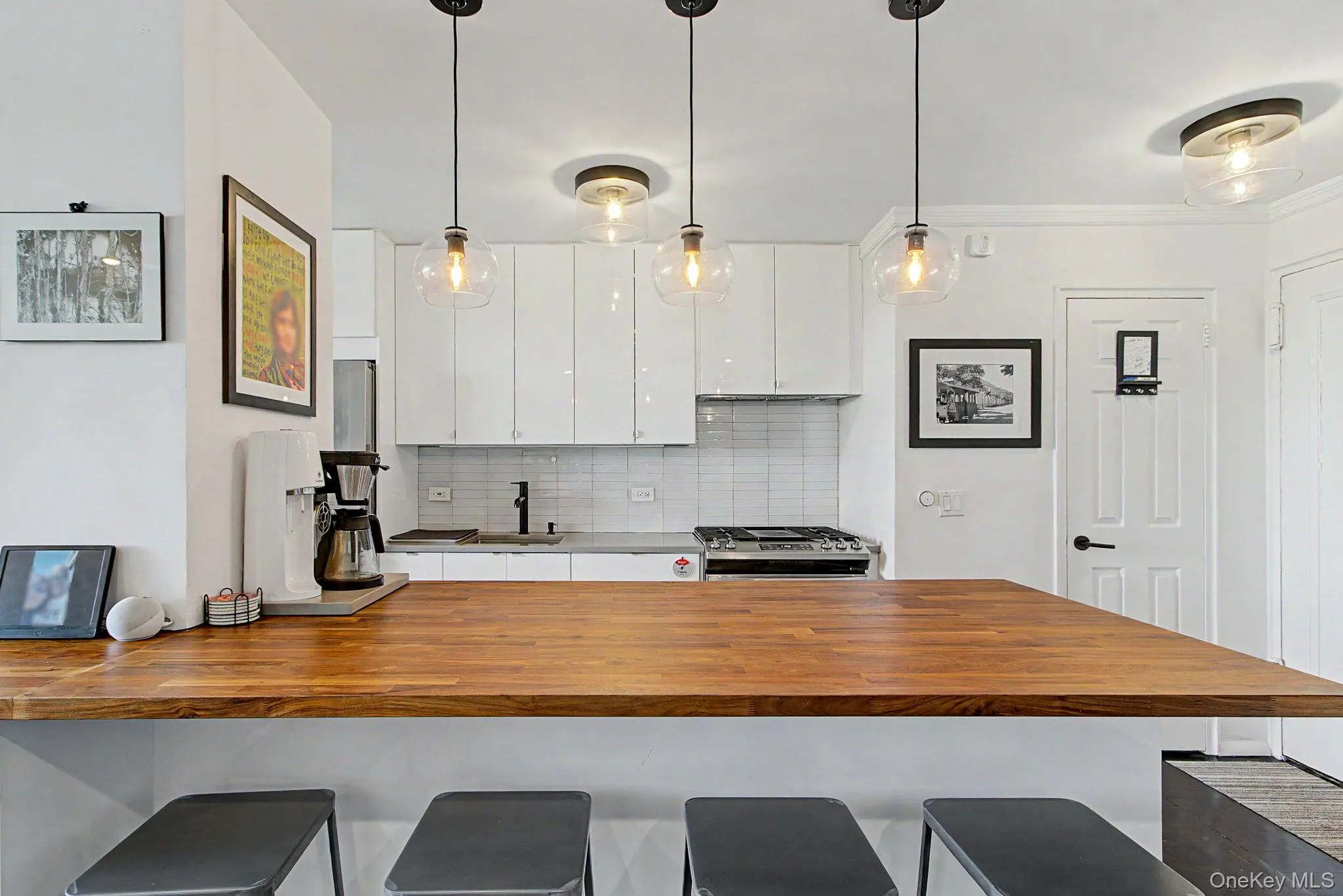 Expansive wood-finish island with seating, complemented by three clear glass pendant lights Expansive wood-finish island with seating, complemented by three clear glass pendant lights