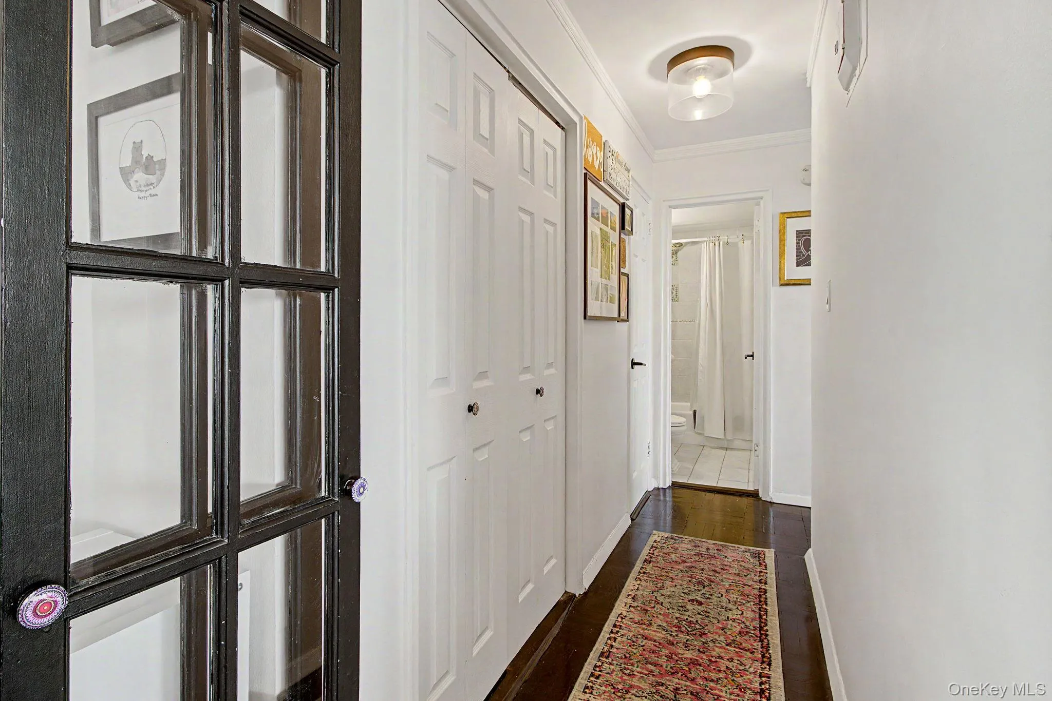 Hallway with dark wood-finish flooring, white walls, and a modern ceiling light fixture Hallway with dark wood-finish flooring, white walls, and a modern ceiling light fixture