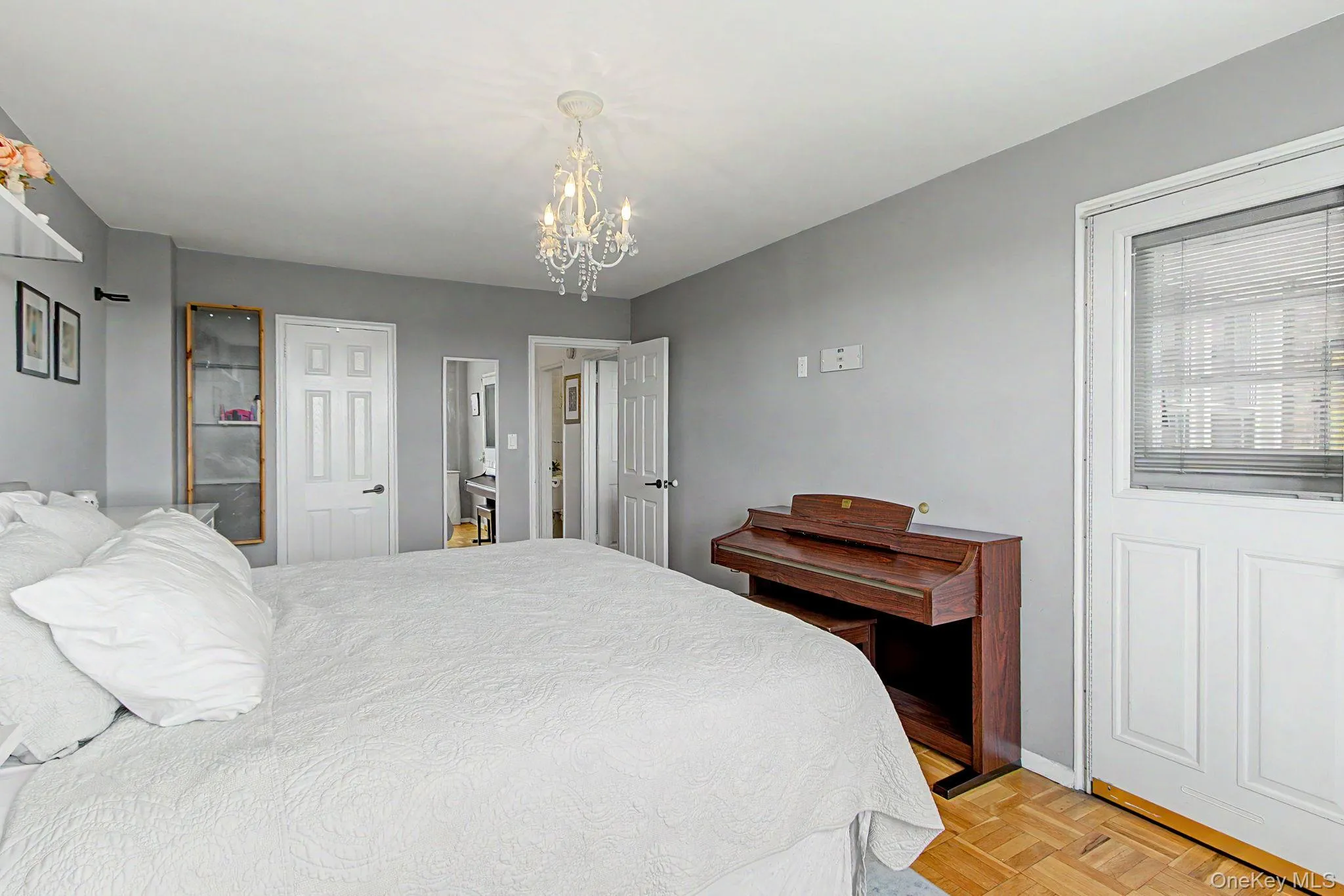 Bedroom featuring wood-finish parquet flooring, a crystal chandelier, and a white paneled door with integrated blinds Bedroom featuring wood-finish parquet flooring, a crystal chandelier, and a white paneled door with integrated blinds