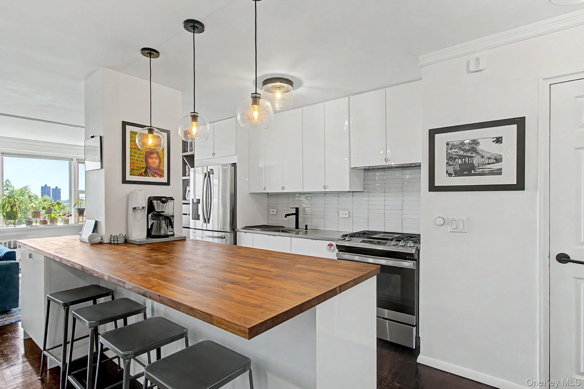 Kitchen featuring a wood-finish peninsula with seating, white high-gloss cabinetry, stainless steel appliances, a tile backsplash, and pendant lighting Kitchen featuring a wood-finish peninsula with seating, white high-gloss cabinetry, stainless steel appliances, a tile backsplash, and pendant lighting