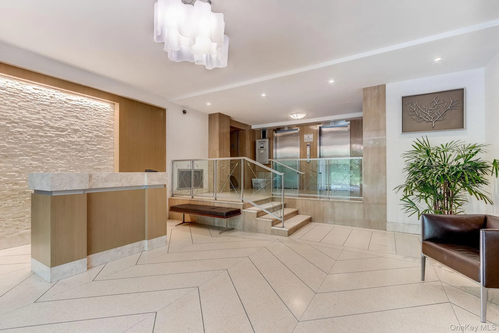 Lobby area featuring a modern reception desk with stone countertop, textured accent wall, statement overhead lighting, and chevron-patterned flooring Lobby area featuring a modern reception desk with stone countertop, textured accent wall, statement overhead lighting, and chevron-patterned flooring