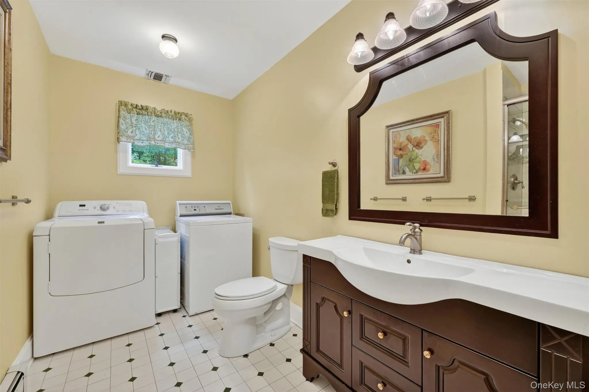 Bathroom featuring a dark wood vanity with a single integrated sink, a large decorative mirror, and a three-light fixture Bathroom featuring a dark wood vanity with a single integrated sink, a large decorative mirror, and a three-light fixture