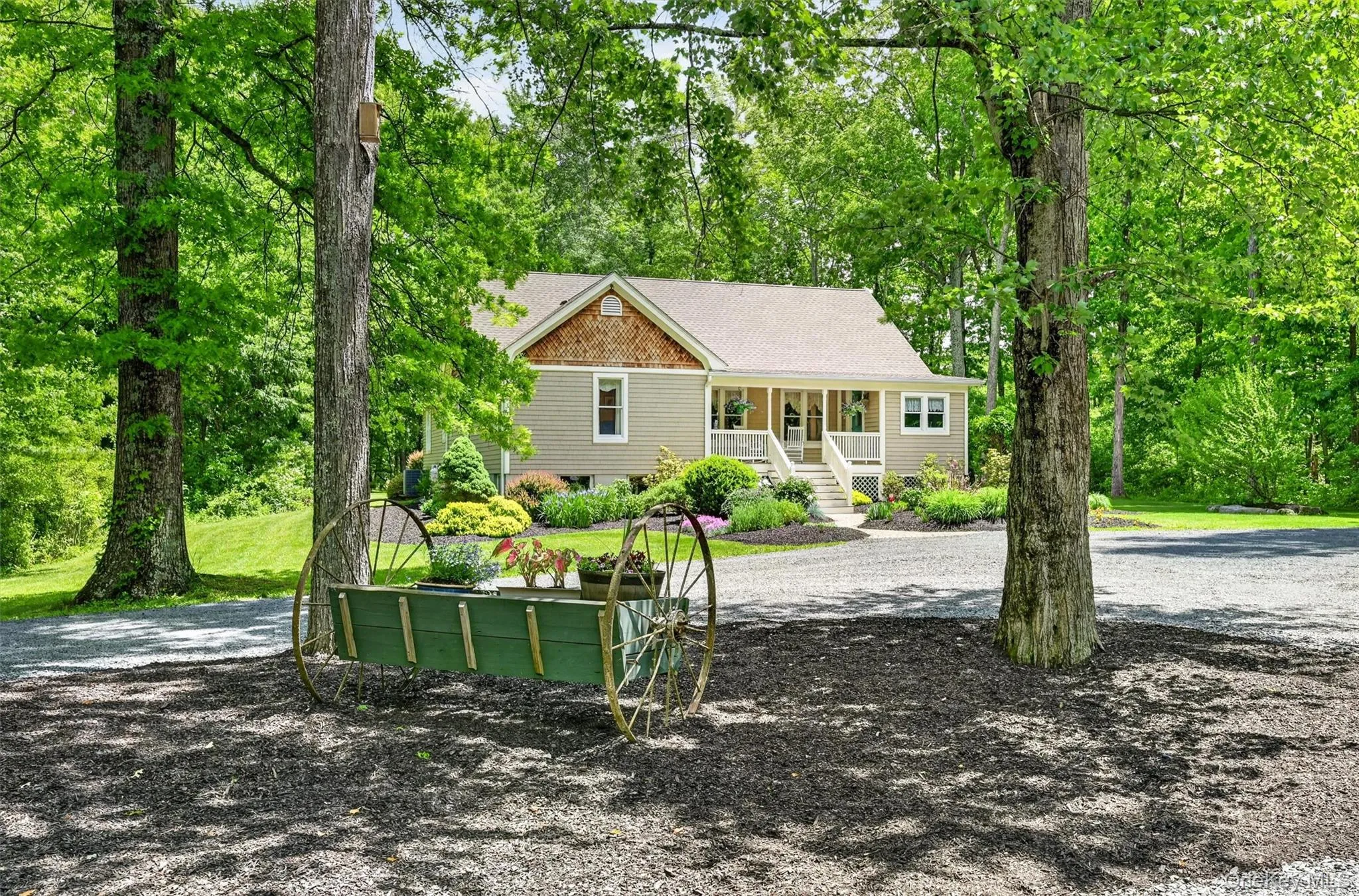 Charming home exterior featuring a covered porch, shake siding accents, and a gravel driveway surrounded by mature trees and landscaping Charming home exterior featuring a covered porch, shake siding accents, and a gravel driveway surrounded by mature trees and landscaping
