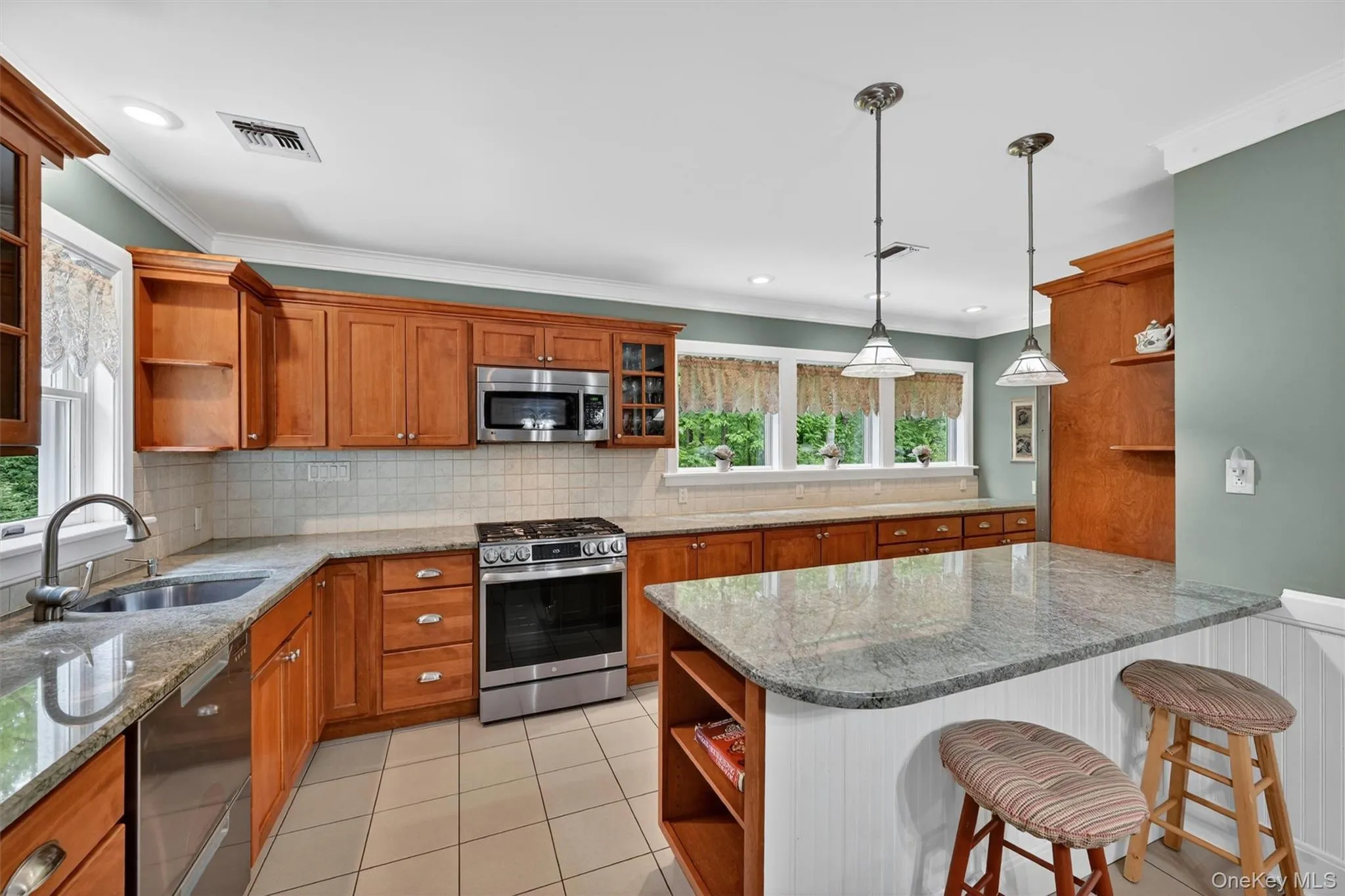 Kitchen featuring wood cabinetry, stainless steel appliances, a center island with countertop, tile flooring, and pendant lighting Kitchen featuring wood cabinetry, stainless steel appliances, a center island with countertop, tile flooring, and pendant lighting