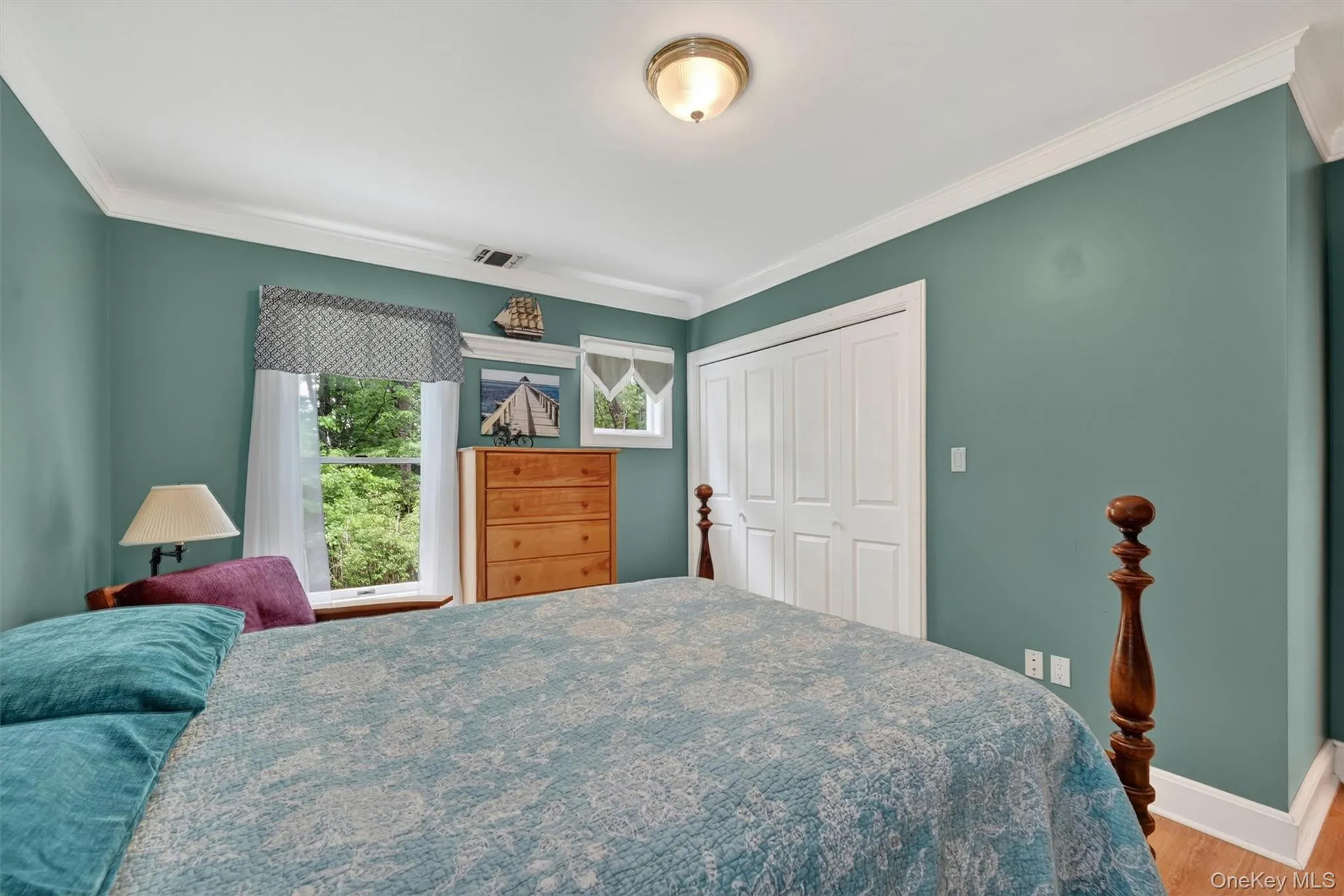 Bedroom featuring a window with natural light, bi-fold closet doors, crown molding, and wood-finish flooring Bedroom featuring a window with natural light, bi-fold closet doors, crown molding, and wood-finish flooring