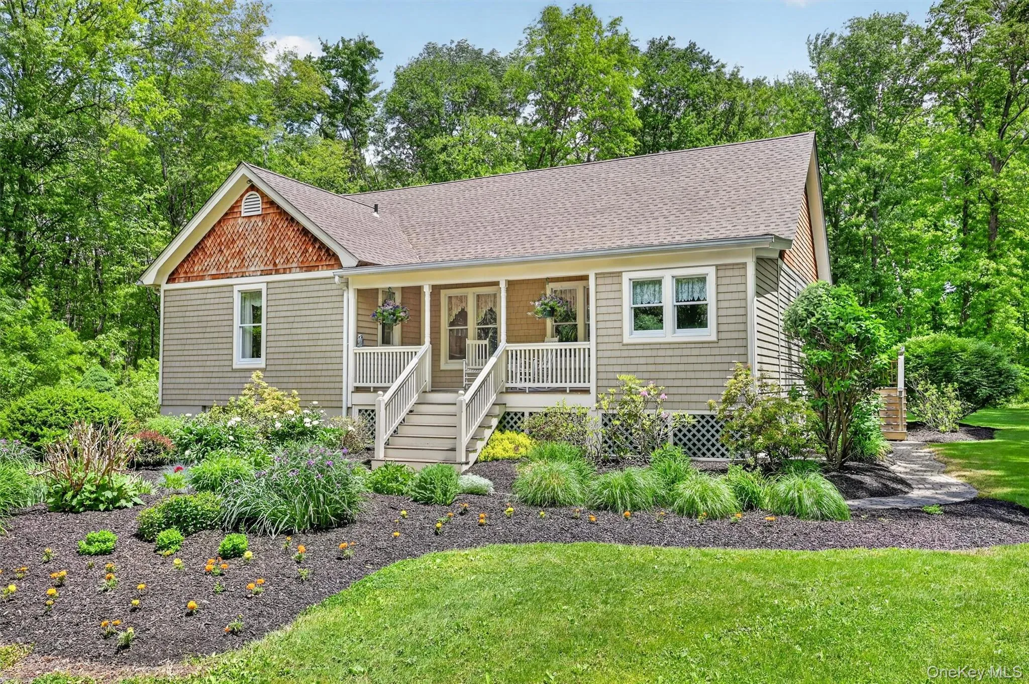 Ranch home featuring a covered front porch with white railings, a front gable with decorative shingle siding, a stone pathway, and extensive landscaping with mature plantings Ranch home featuring a covered front porch with white railings, a front gable with decorative shingle siding, a stone pathway, and extensive landscaping with mature plantings