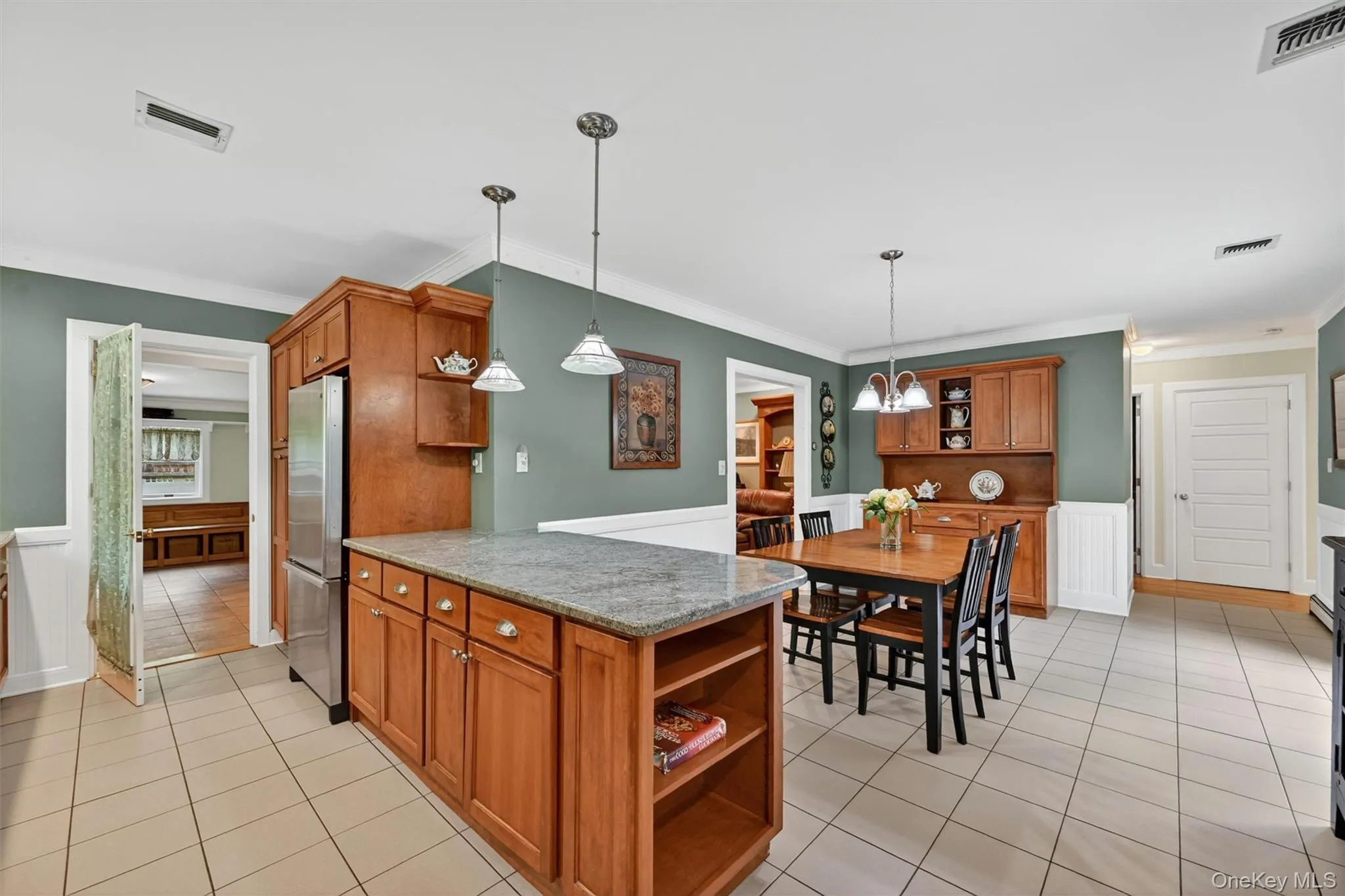 Kitchen featuring a central island with a stone countertop, wood-finish cabinetry, tile flooring, and wainscoting Kitchen featuring a central island with a stone countertop, wood-finish cabinetry, tile flooring, and wainscoting