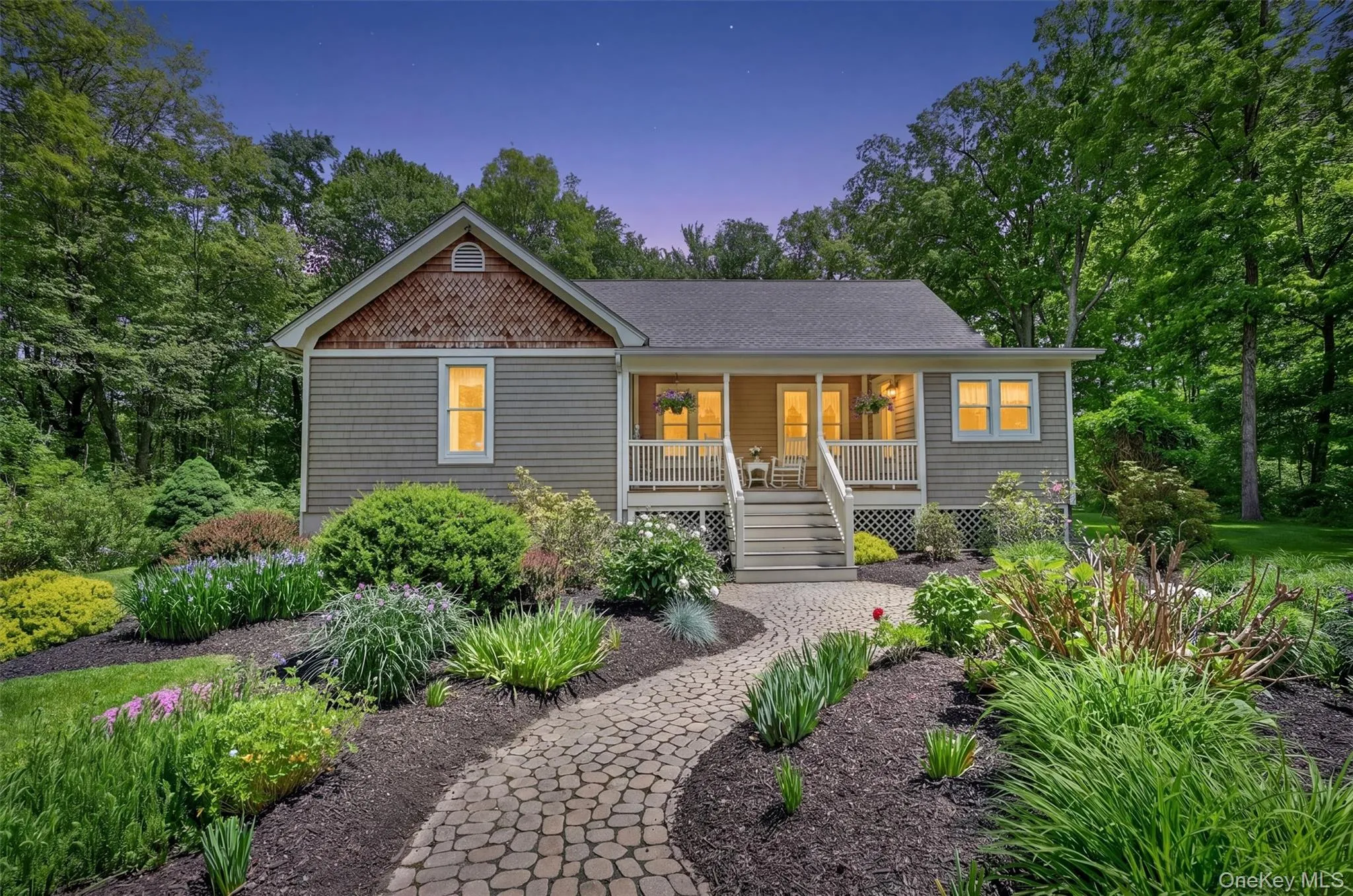 Charming residence featuring a covered front porch with white railings and steps, and a shingled gable accent Charming residence featuring a covered front porch with white railings and steps, and a shingled gable accent