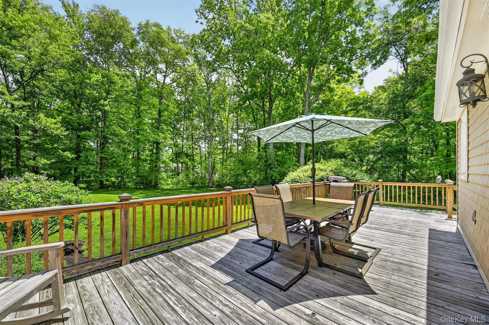 Spacious wood deck with a natural wood railing, featuring a shingled exterior wall with an exterior lantern Spacious wood deck with a natural wood railing, featuring a shingled exterior wall with an exterior lantern