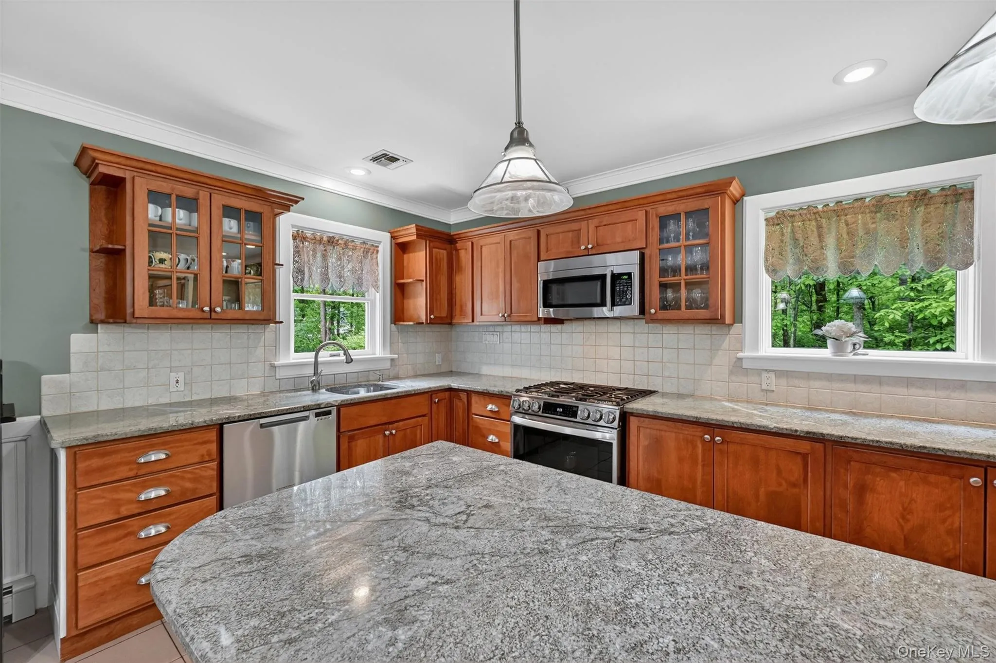 Kitchen featuring a large central island with a granite countertop, wood cabinetry, stainless steel appliances, and a tiled backsplash Kitchen featuring a large central island with a granite countertop, wood cabinetry, stainless steel appliances, and a tiled backsplash
