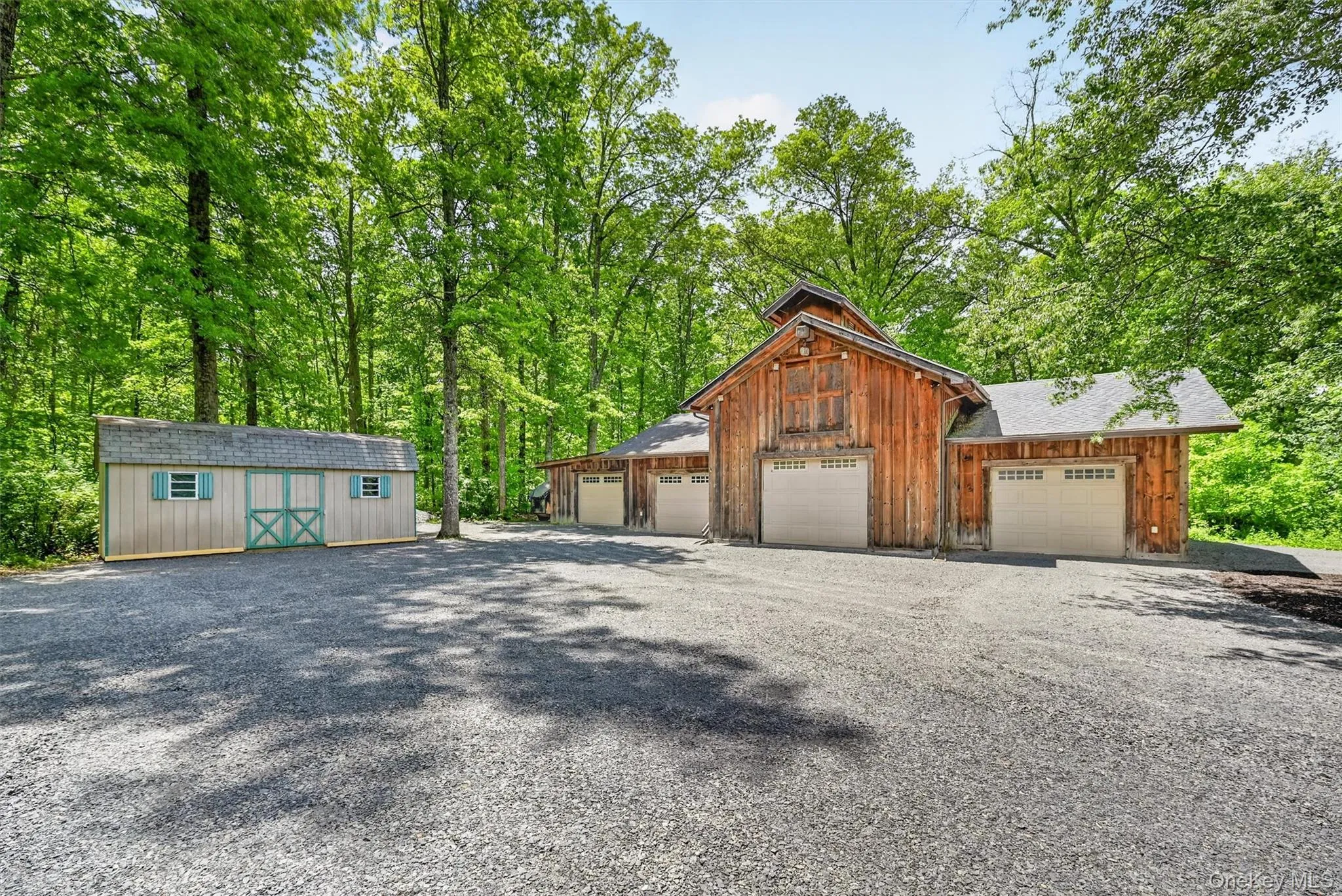 Spacious detached garage/barn with multiple bays, gravel parking area, and additional storage shed, surrounded by a private wooded setting. Spacious detached garage/barn with multiple bays, gravel parking area, and additional storage shed, surrounded by a private wooded setting.