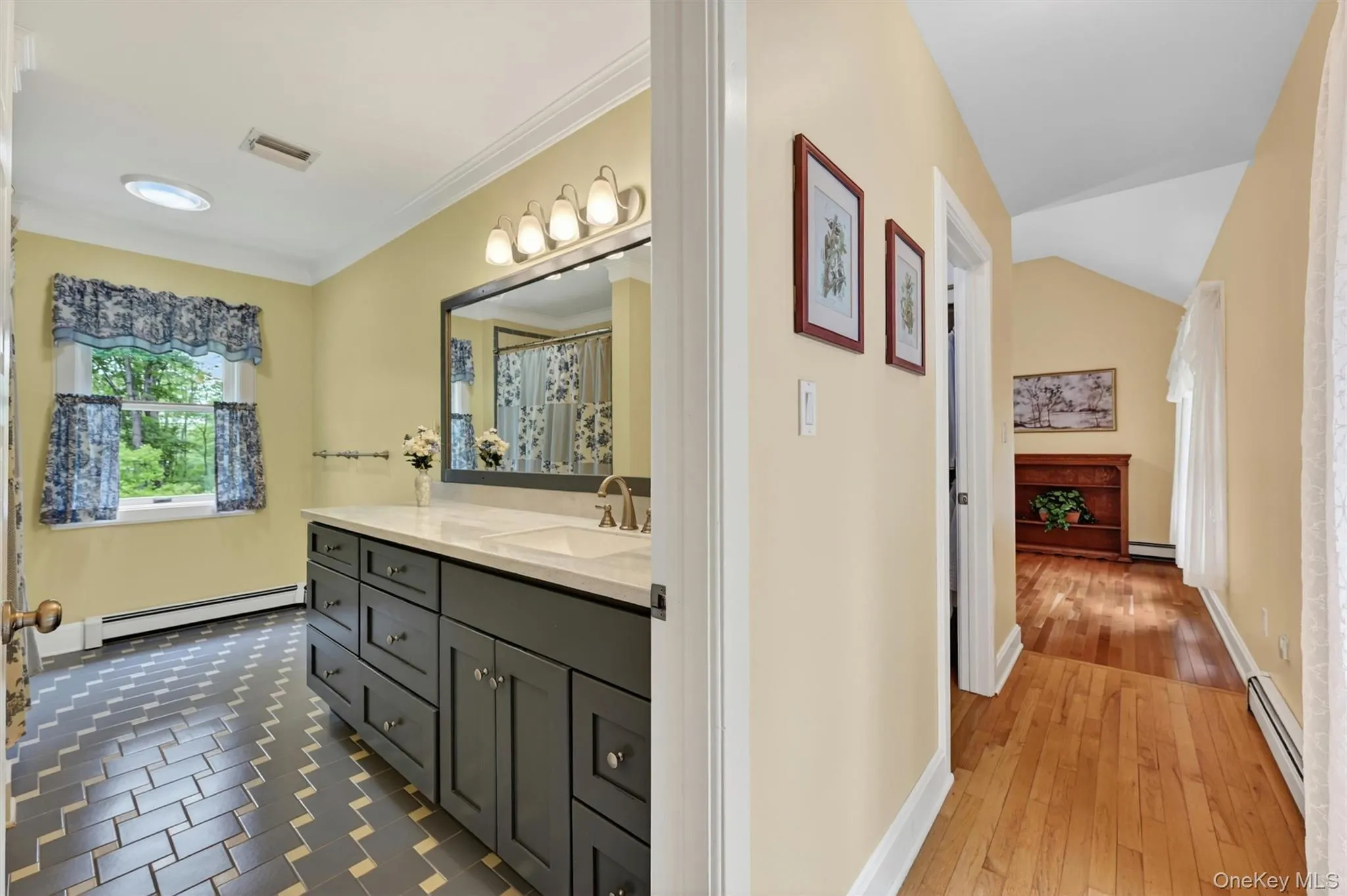Bathroom featuring a dual vanity with white countertop, subway tile flooring in a chevron pattern, and a circular skylight Bathroom featuring a dual vanity with white countertop, subway tile flooring in a chevron pattern, and a circular skylight