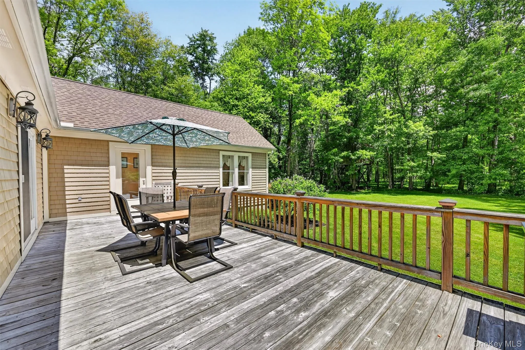 Expansive wood-finish deck with wood railing, featuring a shingle-sided exterior and a lush green lawn surrounded by mature trees Expansive wood-finish deck with wood railing, featuring a shingle-sided exterior and a lush green lawn surrounded by mature trees