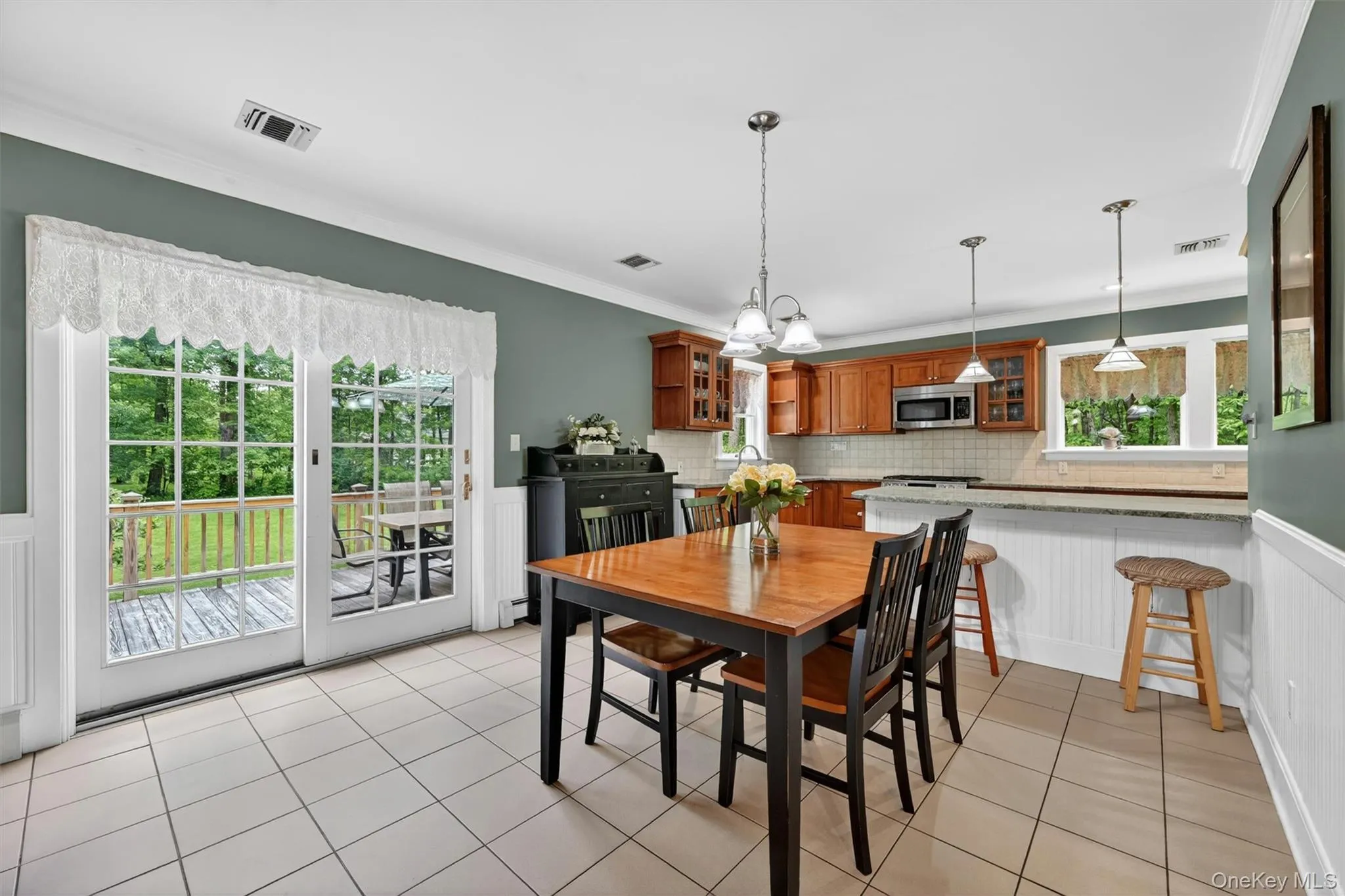 Open-concept kitchen and dining area featuring tile flooring, French doors leading to a deck, wood-finish cabinetry, and a peninsula with countertop seating Open-concept kitchen and dining area featuring tile flooring, French doors leading to a deck, wood-finish cabinetry, and a peninsula with countertop seating