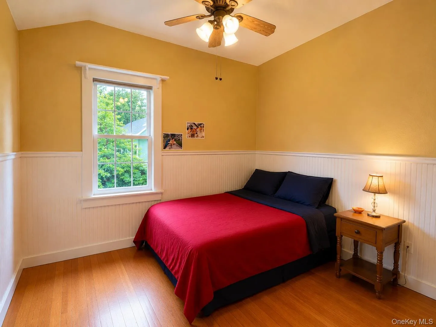 Room featuring beadboard wainscoting, wood-finish flooring, and a single-hung window with exterior greenery visible Room featuring beadboard wainscoting, wood-finish flooring, and a single-hung window with exterior greenery visible