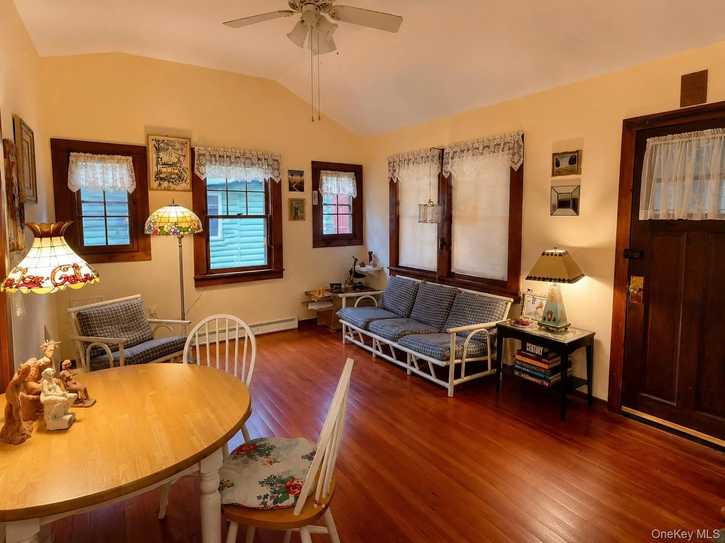 Warm interior featuring wood-finish flooring, multiple windows with dark wood trim, a vaulted ceiling, and a ceiling fan Warm interior featuring wood-finish flooring, multiple windows with dark wood trim, a vaulted ceiling, and a ceiling fan
