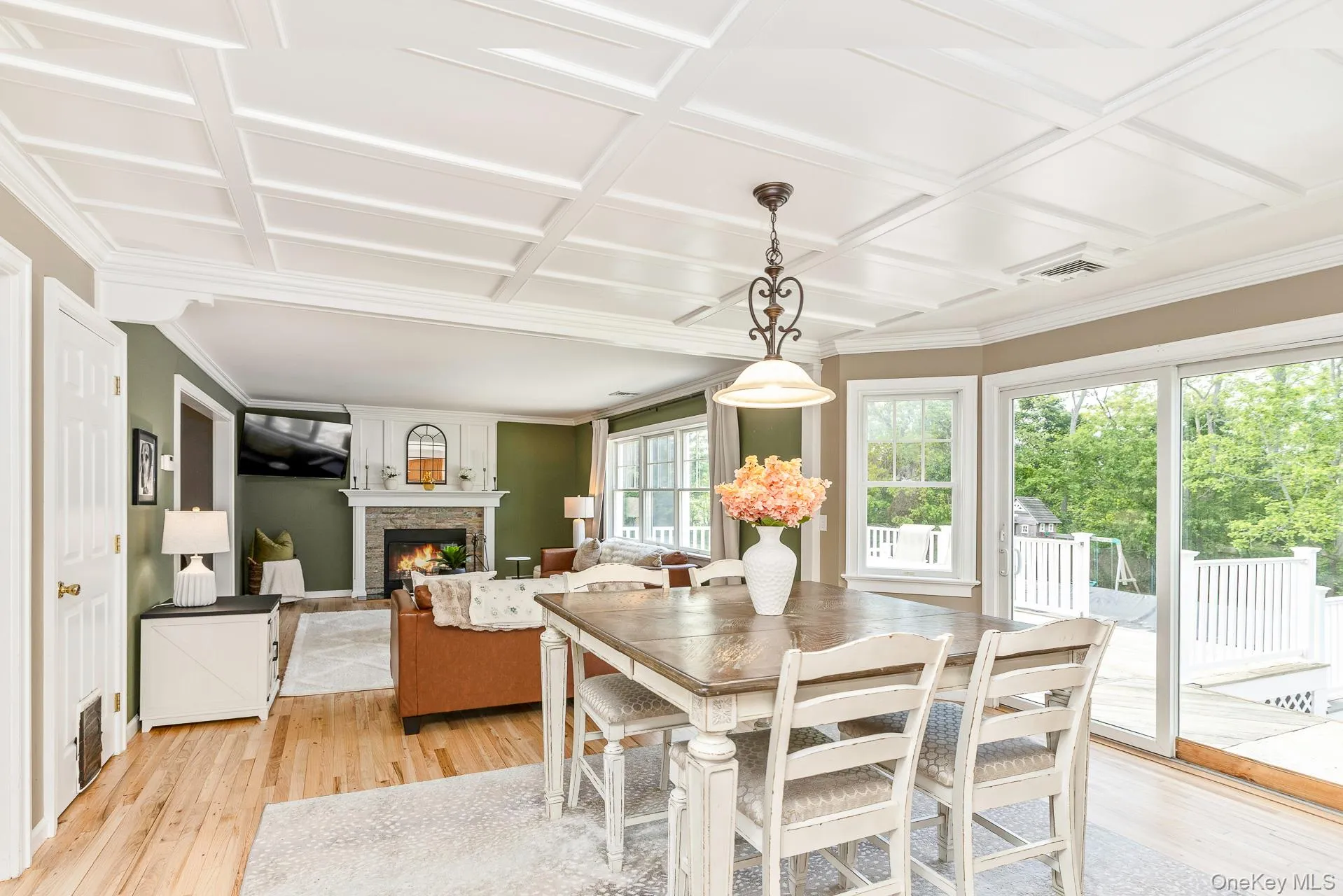 Open-concept living area featuring a coffered ceiling, wood-finish flooring, and a stone-surround fireplace with a white mantel Open-concept living area featuring a coffered ceiling, wood-finish flooring, and a stone-surround fireplace with a white mantel