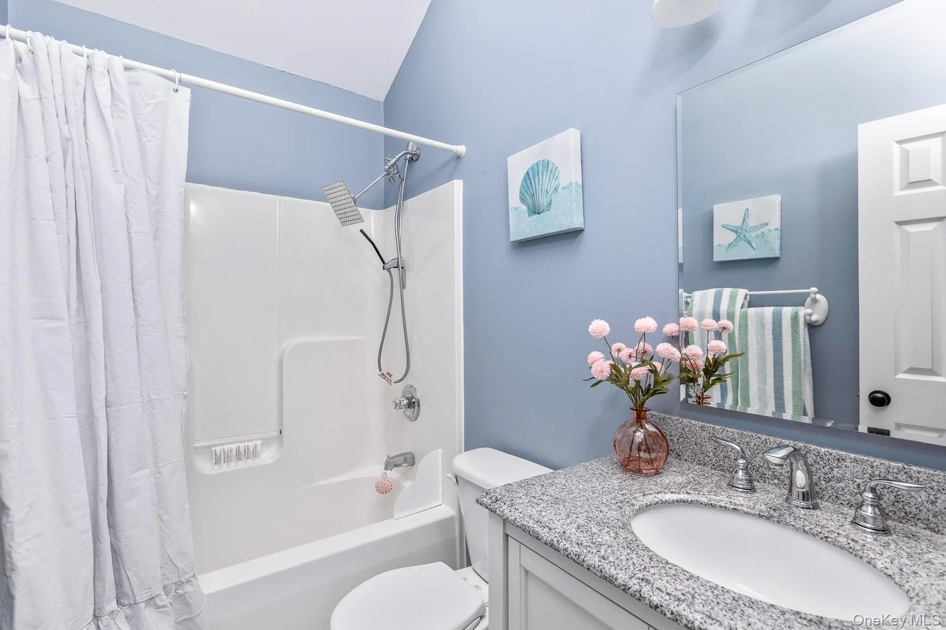 Bathroom featuring a white bathtub and shower combination with a modern showerhead, a toilet, a vanity with a granite countertop, and a built-in mirror Bathroom featuring a white bathtub and shower combination with a modern showerhead, a toilet, a vanity with a granite countertop, and a built-in mirror