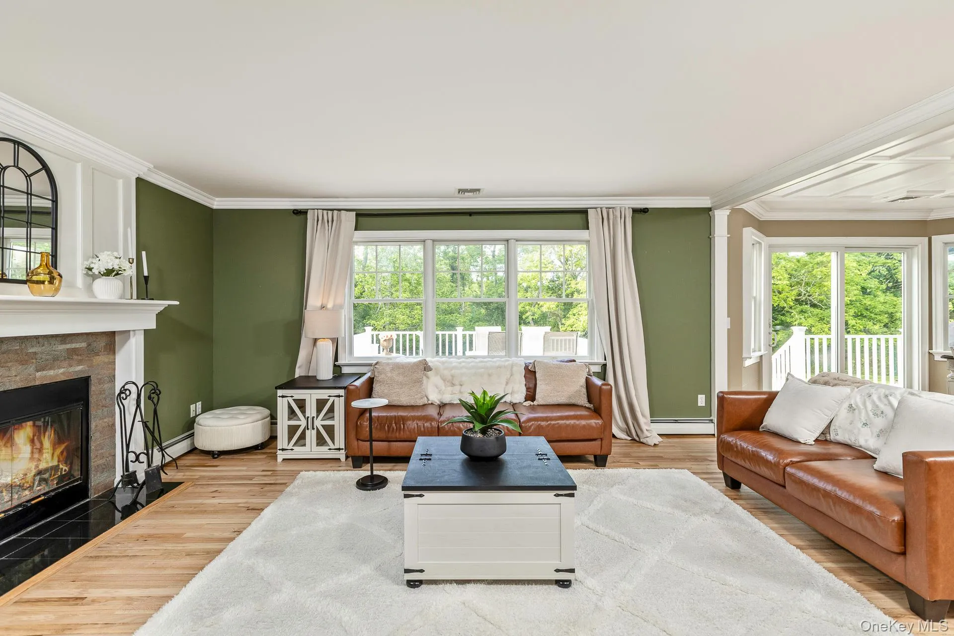 Living area with wood-finish flooring, a stone-faced fireplace with a black tile hearth, and crown molding Living area with wood-finish flooring, a stone-faced fireplace with a black tile hearth, and crown molding