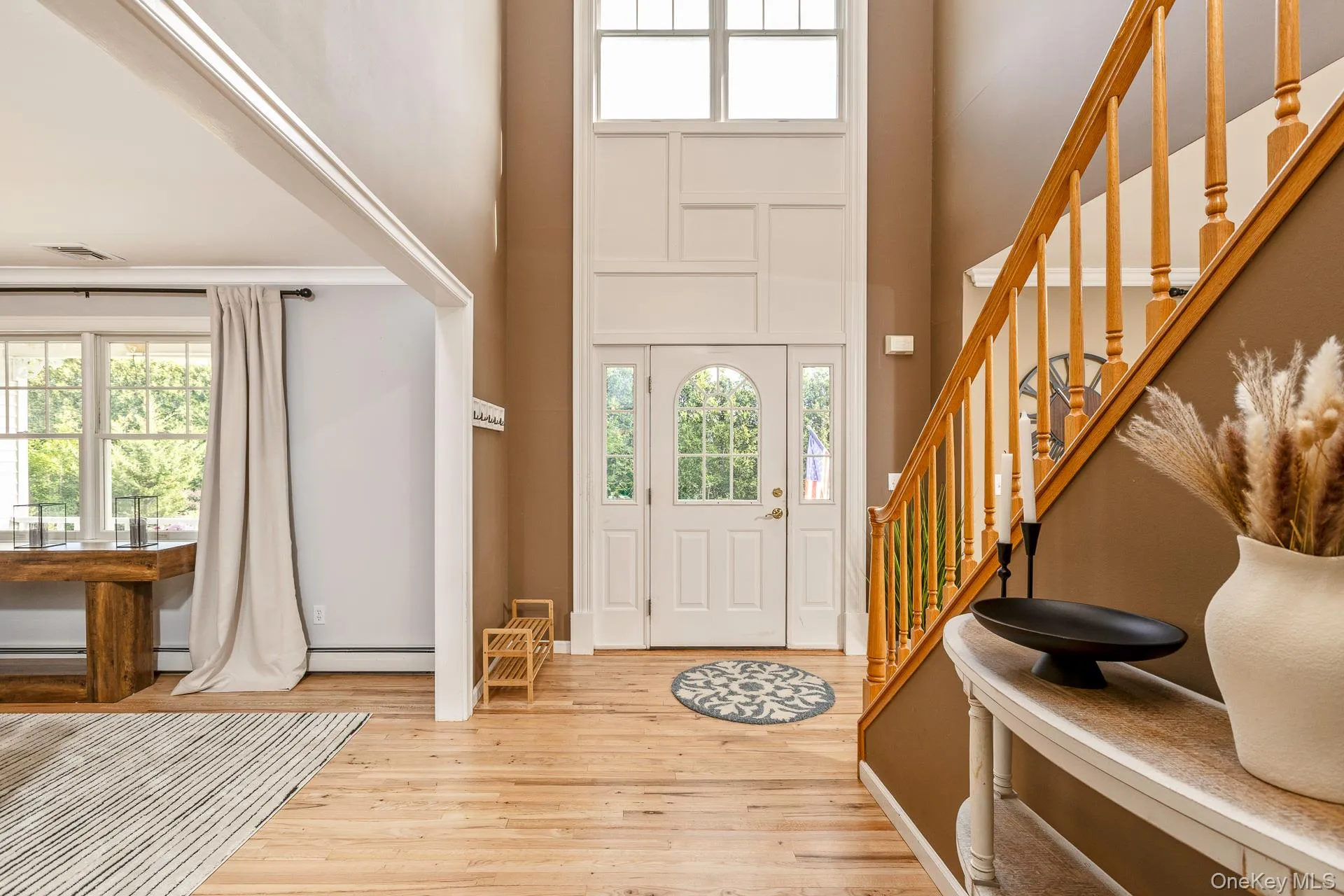 Two-story foyer featuring a light wood staircase with balusters, a front entry door with an arched window, a side panel window, and light wood-finish flooring Two-story foyer featuring a light wood staircase with balusters, a front entry door with an arched window, a side panel window, and light wood-finish flooring