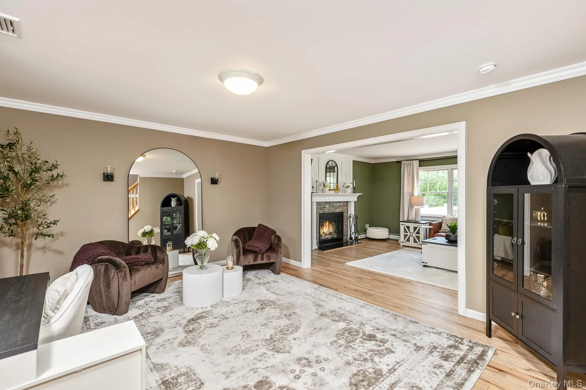 Open-concept interior featuring wood-finish flooring, a neutral wall palette with white crown molding, and an arched doorway framing a fireplace Open-concept interior featuring wood-finish flooring, a neutral wall palette with white crown molding, and an arched doorway framing a fireplace