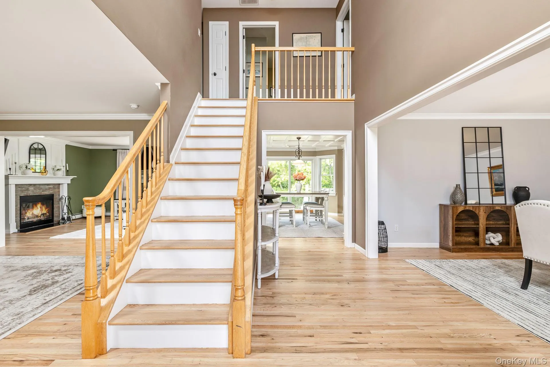 Two-story foyer featuring hardwood flooring, a white staircase with wood-finish handrails, and an upper-level balcony Two-story foyer featuring hardwood flooring, a white staircase with wood-finish handrails, and an upper-level balcony