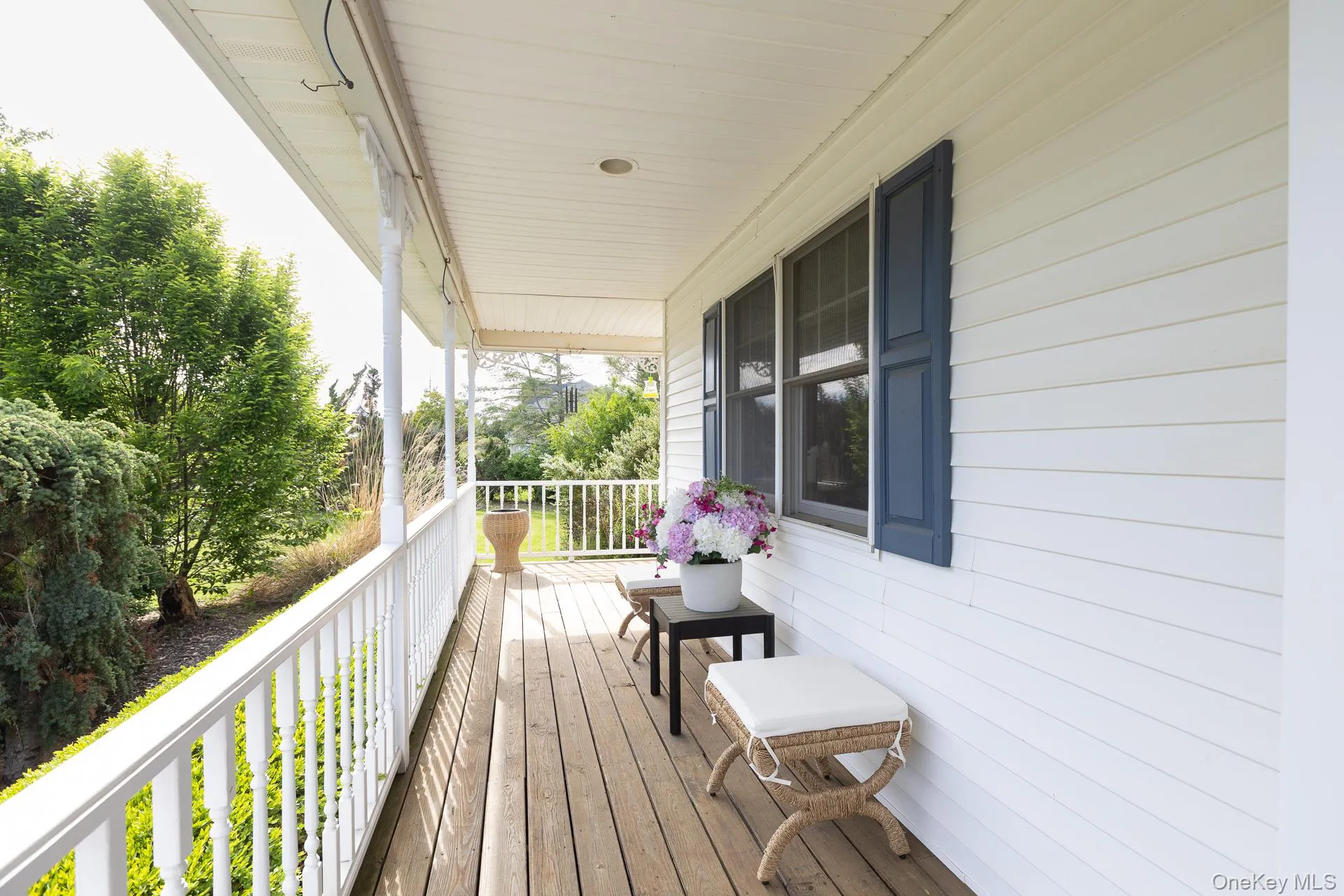 Covered porch with wood-finish flooring, white spindle railing, white vinyl siding, and blue louvered shutters Covered porch with wood-finish flooring, white spindle railing, white vinyl siding, and blue louvered shutters