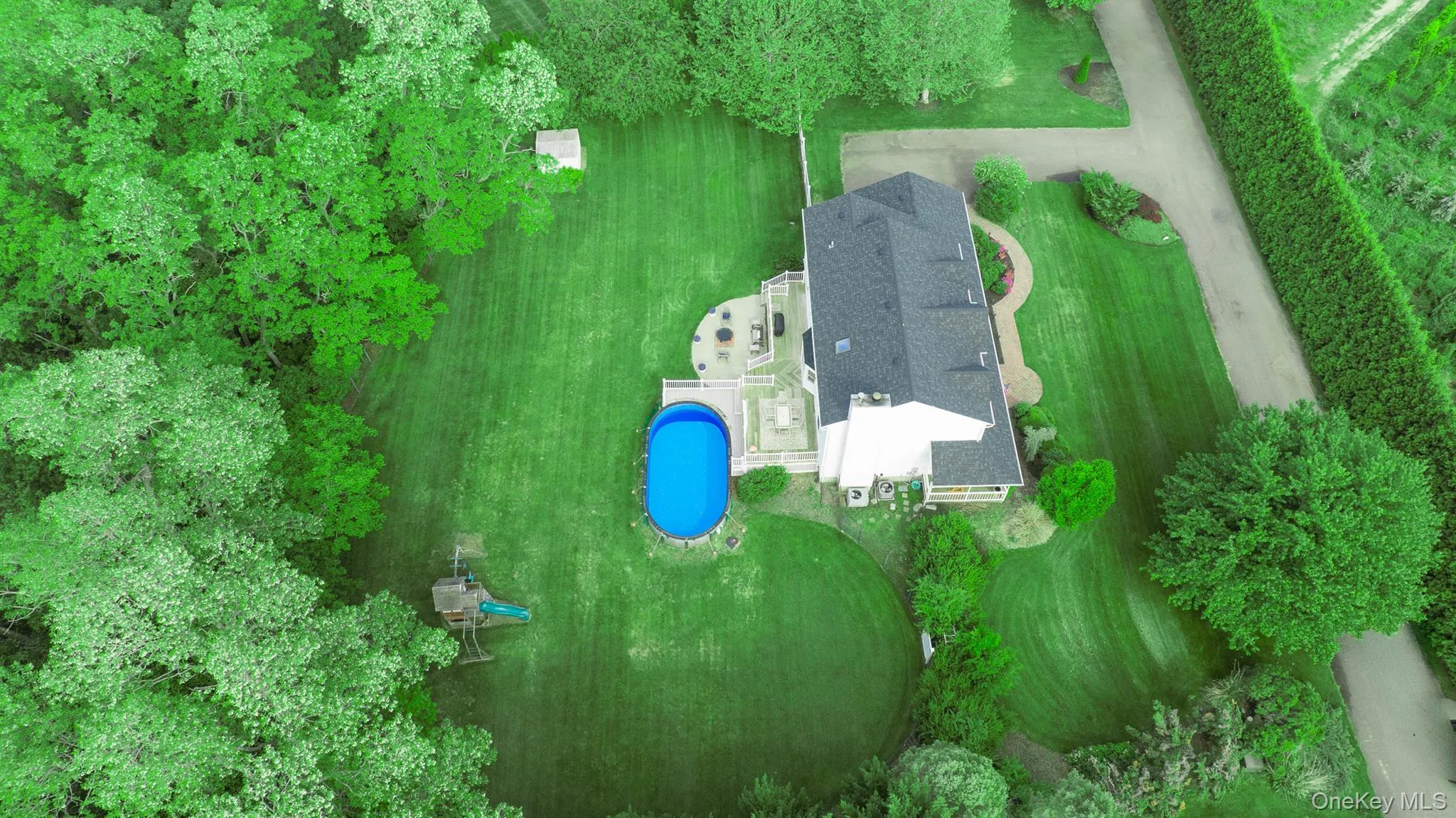 Expansive property featuring a residence with a dark shingled roof, extensive green lawn, and mature trees Expansive property featuring a residence with a dark shingled roof, extensive green lawn, and mature trees