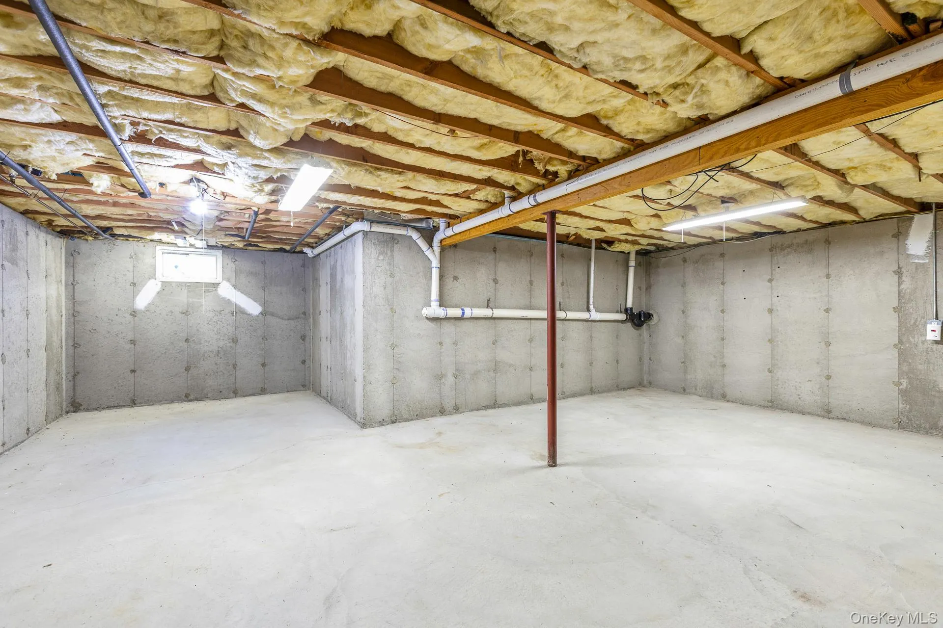 Expansive unfinished basement featuring concrete flooring, exposed concrete walls, visible ceiling insulation, and exposed overhead piping Expansive unfinished basement featuring concrete flooring, exposed concrete walls, visible ceiling insulation, and exposed overhead piping