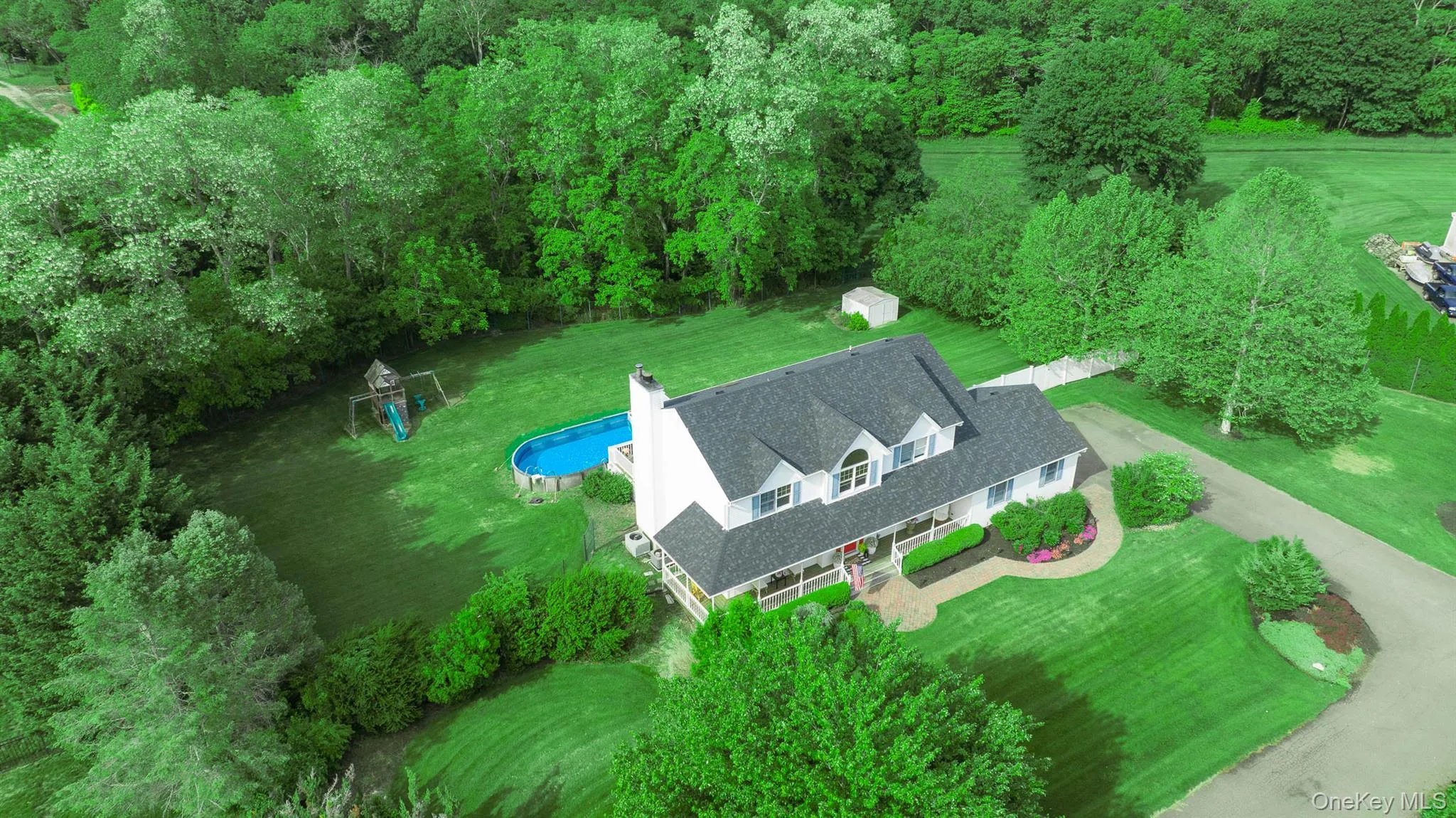 Spacious residential property featuring a white-sided home with a dark shingled roof, extensive green lawns, mature trees, and an above-ground pool Spacious residential property featuring a white-sided home with a dark shingled roof, extensive green lawns, mature trees, and an above-ground pool