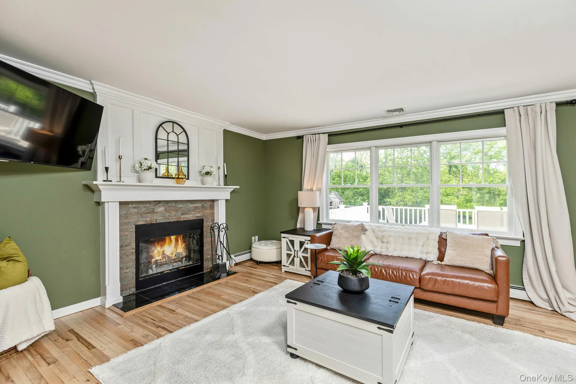 Living area featuring a stone-clad fireplace with a black hearth, hardwood flooring, and crown molding Living area featuring a stone-clad fireplace with a black hearth, hardwood flooring, and crown molding