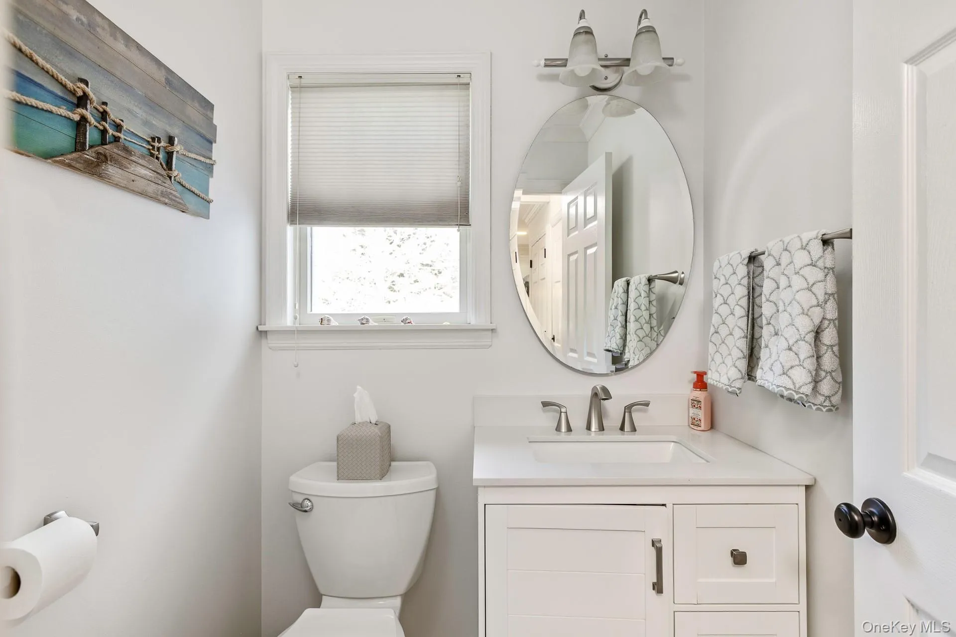 First floor Bathroom featuring white vanity with integrated sink, chrome faucet, oval mirror, and window with privacy blind First floor Bathroom featuring white vanity with integrated sink, chrome faucet, oval mirror, and window with privacy blind