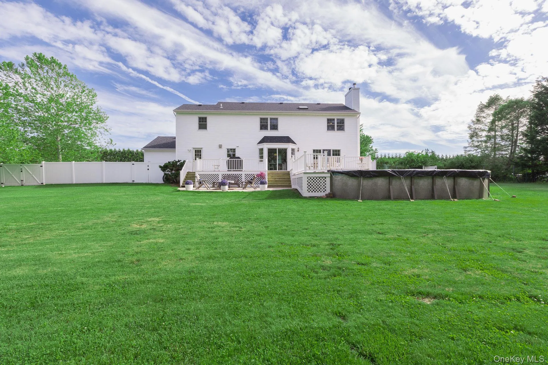Spacious rear yard featuring a large white two-story residence, an elevated composite deck, and an above-ground pool Spacious rear yard featuring a large white two-story residence, an elevated composite deck, and an above-ground pool