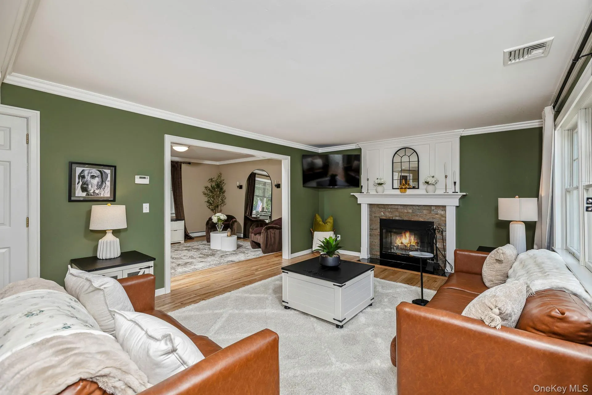 Living area featuring a stone fireplace with a white mantel, wide cased opening, crown molding, and hardwood flooring Living area featuring a stone fireplace with a white mantel, wide cased opening, crown molding, and hardwood flooring