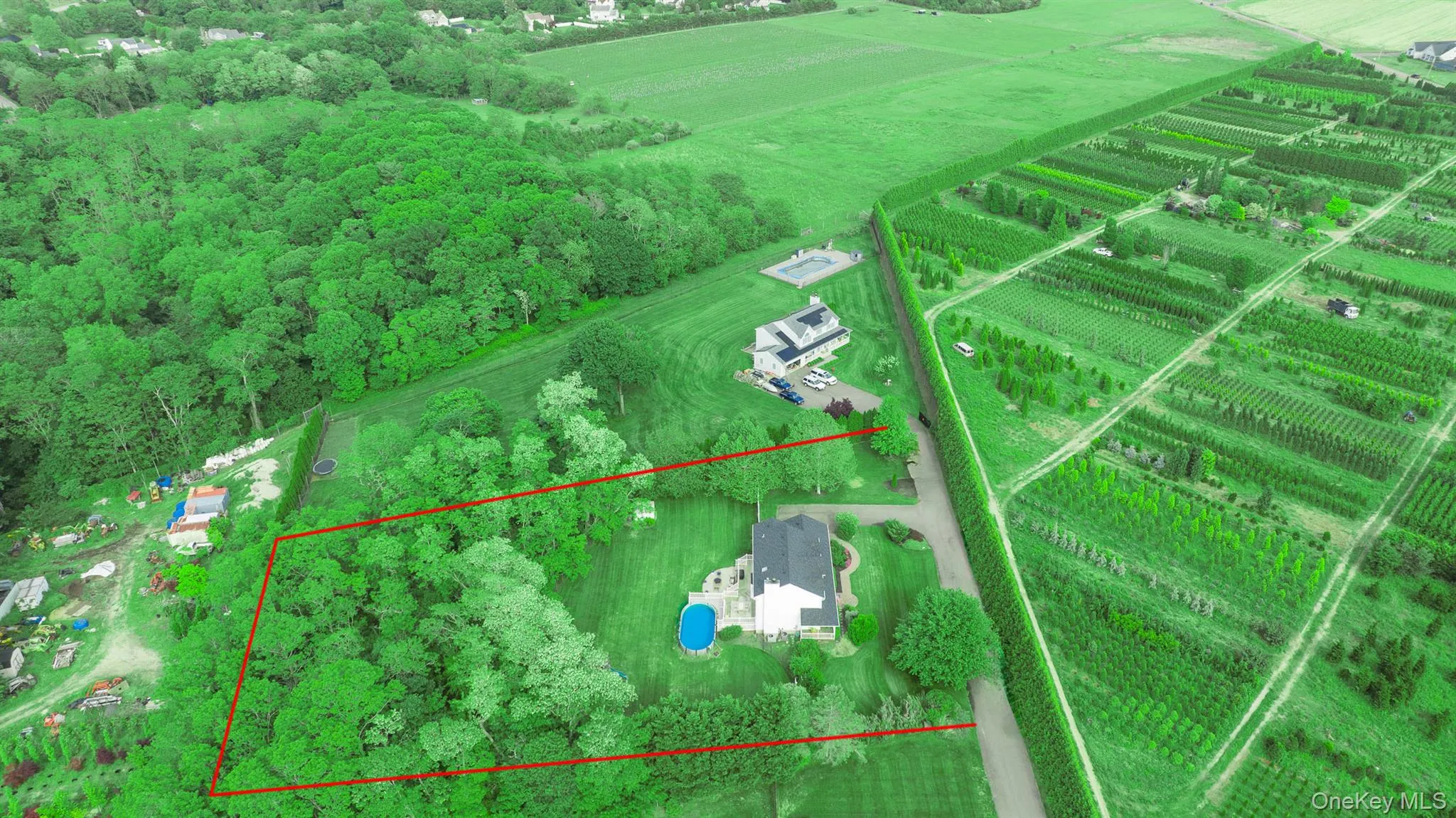 Expansive aerial property featuring a single-family home with a dark roof and light-colored siding, a circular above-ground pool, and a gravel driveway Expansive aerial property featuring a single-family home with a dark roof and light-colored siding, a circular above-ground pool, and a gravel driveway