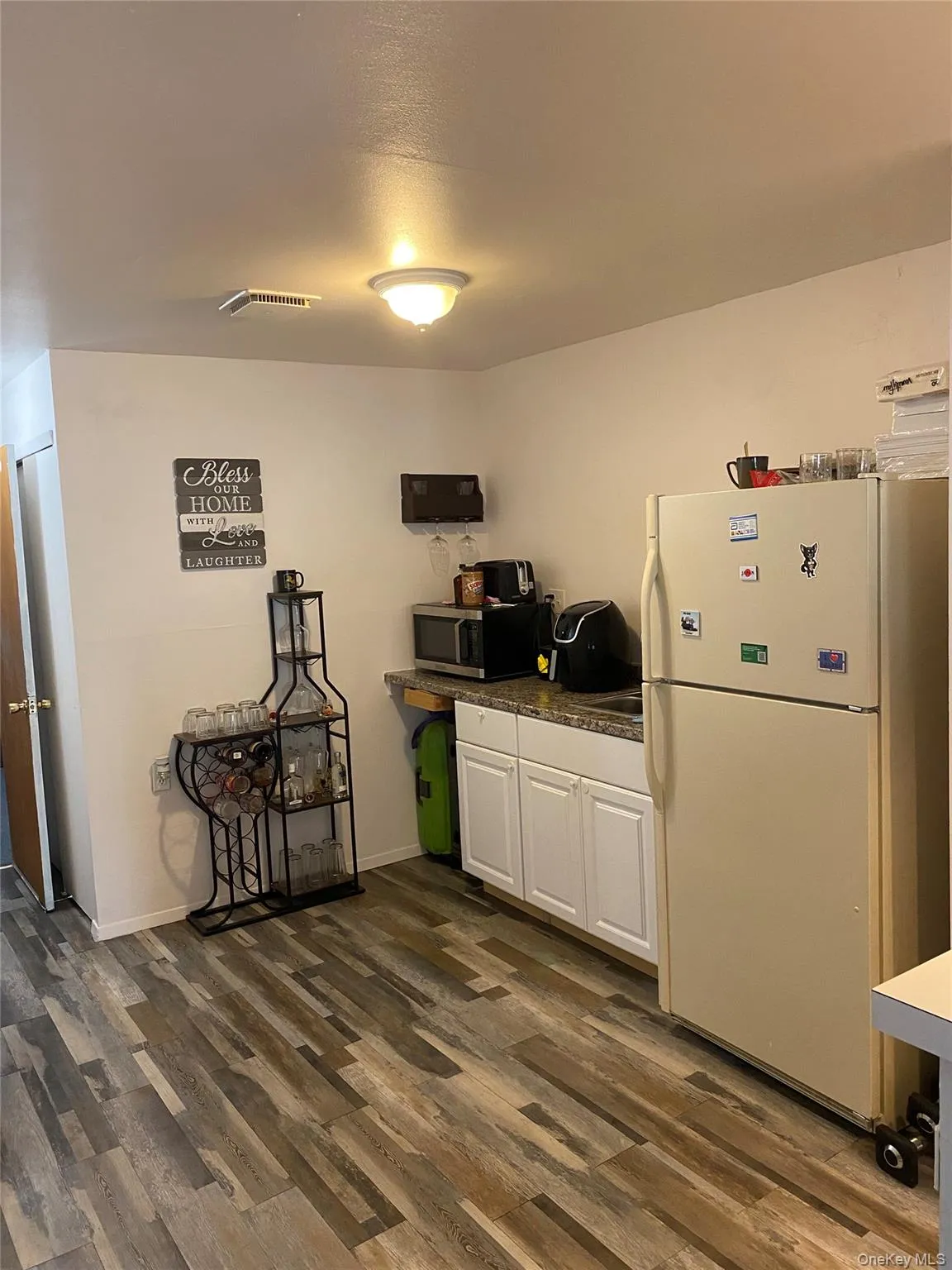 Kitchen with white cabinets, dark countertops, dark wood-type flooring, freestanding refrigerator, and stainless steel microwave Kitchen with white cabinets, dark countertops, dark wood-type flooring, freestanding refrigerator, and stainless steel microwave