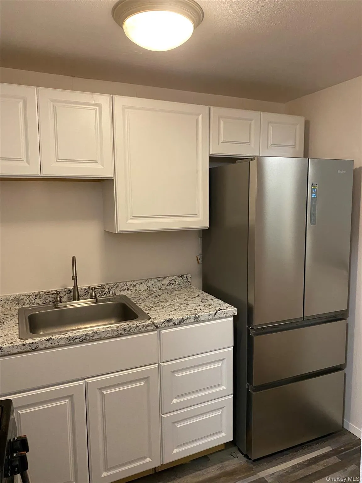 Kitchen featuring dark wood finished floors, freestanding refrigerator, white cabinetry, and a sink Kitchen featuring dark wood finished floors, freestanding refrigerator, white cabinetry, and a sink
