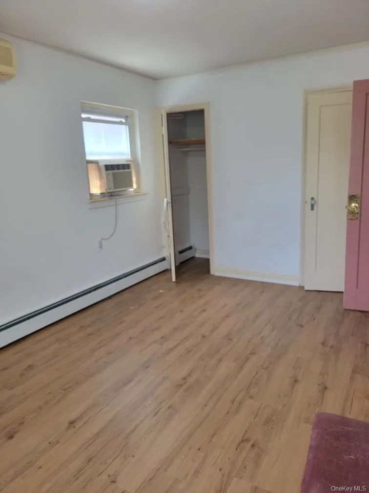 Unfurnished bedroom featuring an AC wall unit, light wood-style floors, baseboards, cooling unit, and a baseboard radiator Unfurnished bedroom featuring an AC wall unit, light wood-style floors, baseboards, cooling unit, and a baseboard radiator
